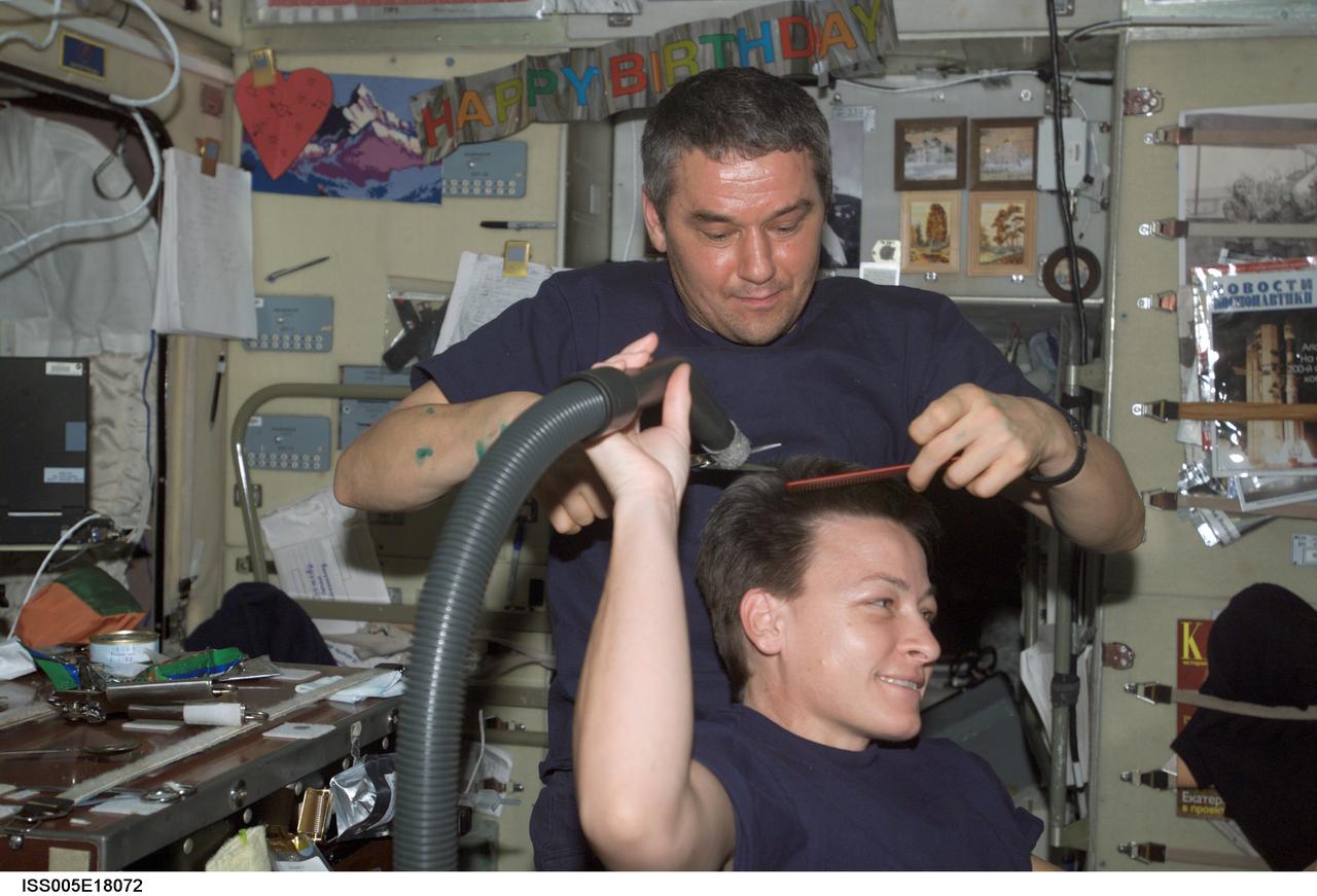 ISS005-E-18072 (October 2002) --- Cosmonaut Valery G. Korzun, Expedition Five mission commander, cuts astronaut Peggy A. Whitson&#0146;s hair in the Zvezda Service Module on the International Space Station (ISS). Whitson, flight engineer, holds a vacuum device the crew has fashioned to garner freshly cut hair, which is floating freely.