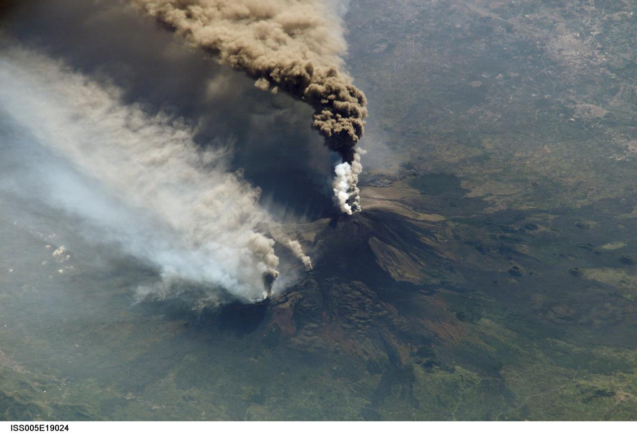 ISS005-E-19024 (30 October 2002) ---  The three-member crew of the Expedition Five  mission onboard the International Space Station was able to observe Mt. Etna&#0146;s spectacular eruption, and photograph the details of the eruption plume and smoke from fires triggered by the lava as it flowed down the 11,000 ft mountain.  This image and a second image (ISS005-E-19016) are looking obliquely to the southeast over the island of Sicily.  The wider view (ISS005-E-19024) shows the ash plume curving out toward the horizon, caught first by low-level winds blowing to the southeast, and to the south toward Africa at higher altitudes.  Ashfall was reported in Libya, more than 350  miles away.  The lighter-colored plumes downslope and north of the summit seen in this frame are produced by forest fires set by lava flowing into the pine forests on the slope of the mountain.   This image provides a more three-dimensional profile of the eruption plume.  This eruption was one of Etna&#0146;s most vigorous in years,  volcanologists reported this week.  The eruption was triggered by a series of earthquakes on October 27, 2002, they said.  These images were taken on October 30.    Although schools were closed and air traffic was diverted because of the ash, no towns or villages were reported to have been threatened by the lava flow.