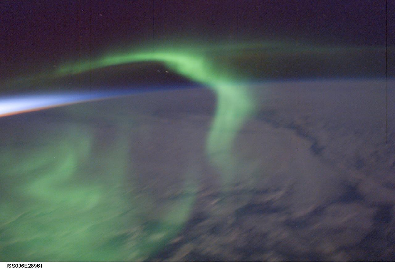 ISS006-E-028961 (16 Feb. 2003) ---  The Expedition Six crew enjoyed this green aurora dancing over the night side of the Earth just after sunset on February 16, 2003. The reds and blues of sunset light up the air layer to the west. The image was recorded  with a 58 mm lens on a digital still camera. Because auroras follow Earth's magnetic field, they are observed at Earth's poles when the oxygen and nitrogen atoms start to glow when bombarded by charged particles coming from the sun.  In a sense, auroras are the "neon lights" of the poles.