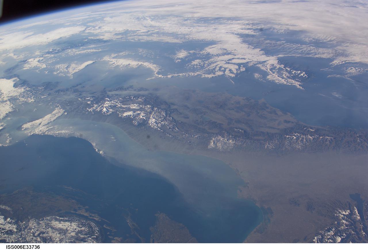 ISS006-E-33736 (25 February 2003) --- The boot of Italy crosses the image in this southwest-looking view taken by an Expedition Six crewmember onboard the International Space Station (ISS). The spine of Italy is highlighted with snow and the largely cloud-covered Mediterranean Sea is at the top. The Adriatic Sea transverses most of the bottom of the image and Sicily appears top left beyond the toe of the boot. The heel lies out of the left side of the image. Corsica and Sardinia appear right of center partly under cloud. The floor of the Po River valley, lower right, is obscured by haze. Experience gained from similar haze events, in which atmospheric pressure, humidity and visibility and atmospheric chemistry were known, suggests that the haze as industrial smog. Industrial haze from the urban region of the central and upper Po valley accumulates to visible concentrations under conditions of high atmospheric pressure and the surrounding mountains prevent easy dispersal. This view illustrates the markedly different color and texture of cloud versus industrial aerosol haze.