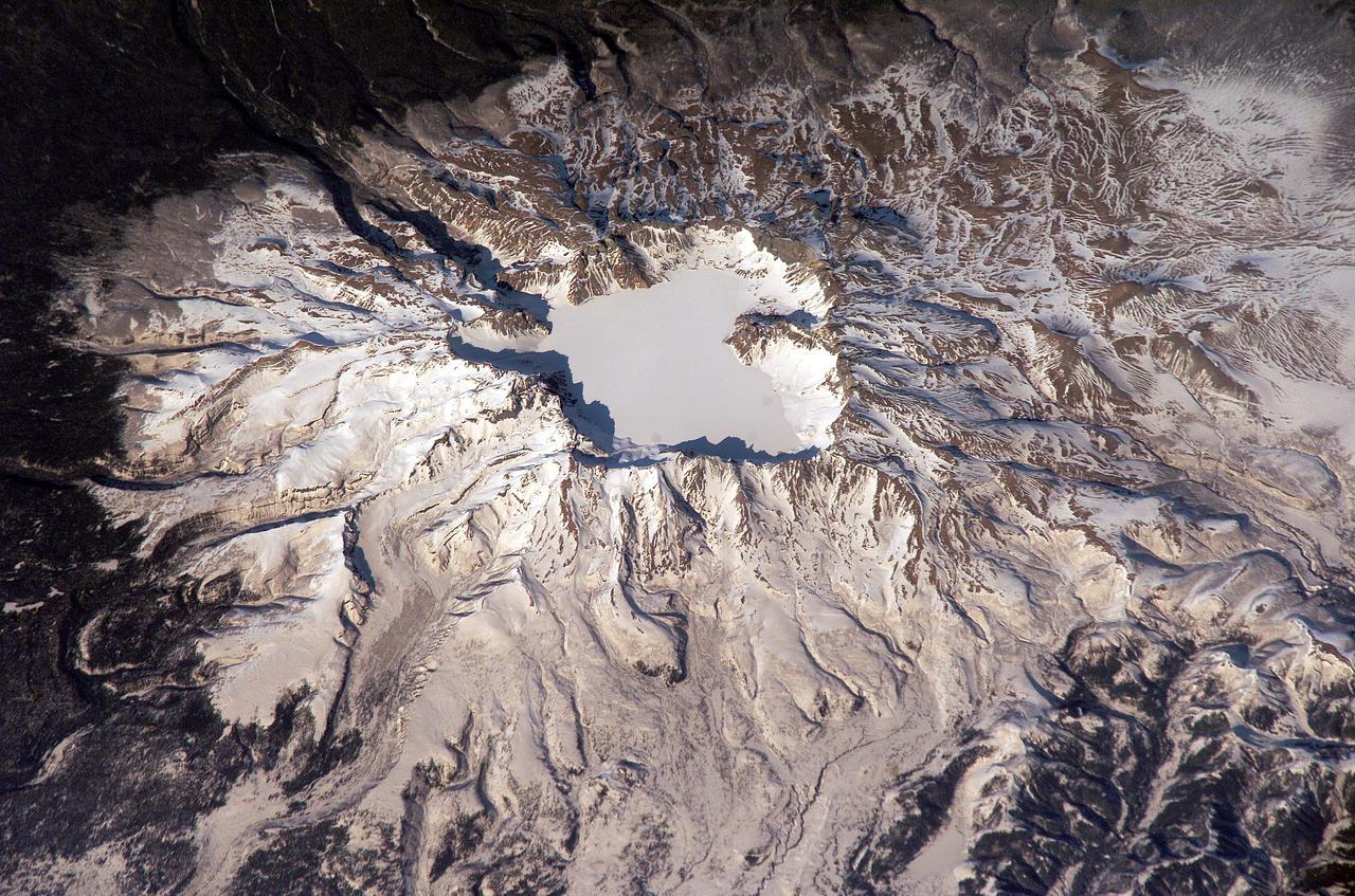 ISS006-E-43366 (4 April 2003) --- This view featuring Baitoushan Volcano, China and North Korea, was photographed by an Expedition 6 crewmember on the International Space Station (ISS). One of the largest known Holocene eruptions occurred at Baitoushan Volcano (also known as Changbaishan in China and P’aektu-san in Korea) about 1000 A.D., with erupted material deposited as far away as northern Japan – a distance of approximately 1200 kilometers. The eruption also created the 4.5 kilometer diameter, 850 meters deep summit caldera of the volcano that is now filled with the waters of Lake Tianchi (or Sky Lake). This oblique photograph was taken during the winter season, and snow highlights frozen Lake Tianchi along with lava flow lobes along the southern face of the volcano. Baitoushan last erupted in 1702 and is considered a dormant volcano. Gas emissions were reported from the summit and nearby hot springs in 1994, but no evidence of renewed activity of the volcano was observed. The Chinese-Korean border runs directly through the center of the summit caldera, and the mountain is considered sacred by the dominantly Korean population living near the volcano. Lake Tianchi is a popular resort destination, both for its natural beauty and alleged sightings of unidentified creatures living in its depths (similar to legendary Loch Ness Monster in Scotland).
