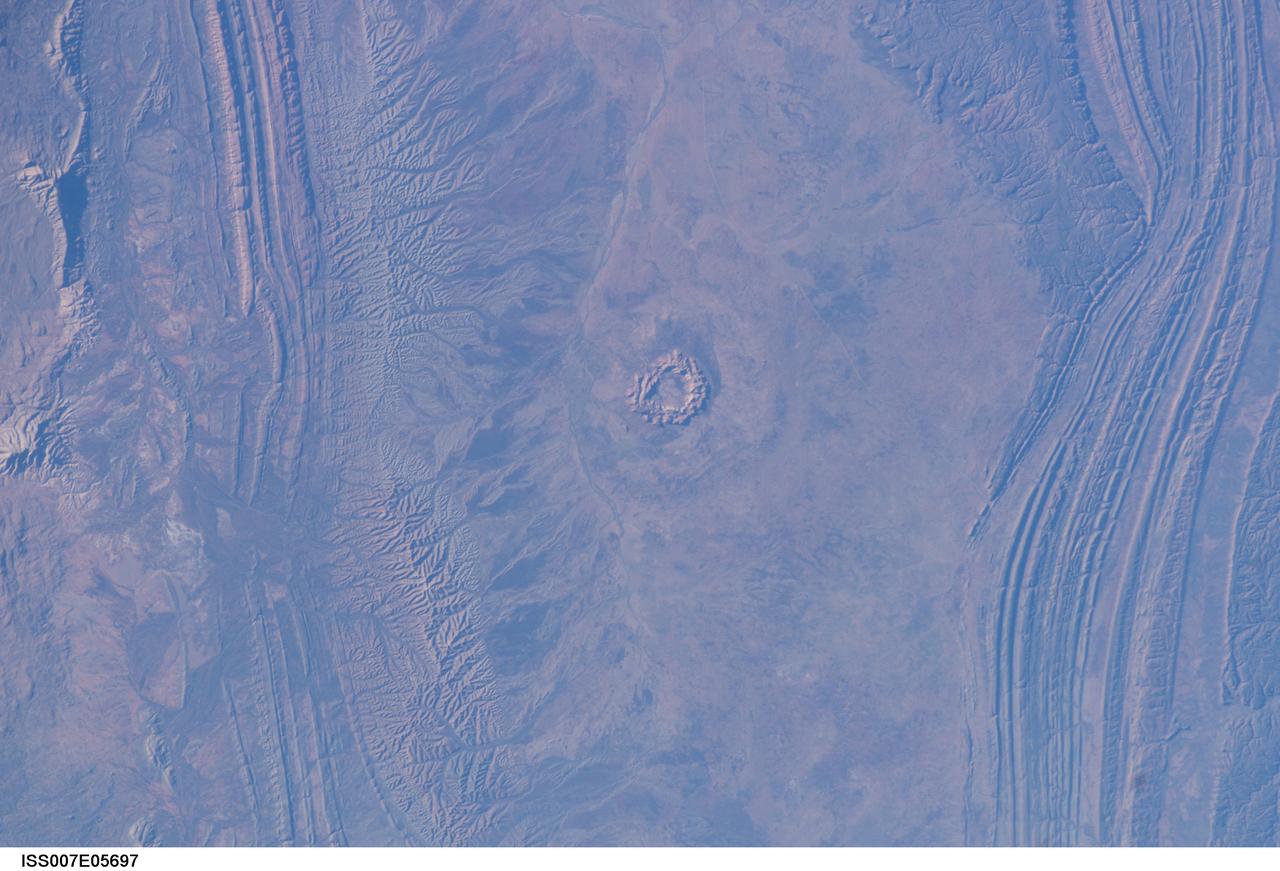ISS007-E-05697 (20 May 2003) --- This image, photographed by an Expedition 7 crewmember onboard the International Space Station (ISS), shows Gosses Bluff, an impact crater sandwiched between the MacDonnell Range to the north and the James Range to the south in Australia’s Northern Territory – it is about 160 kilometers west of Alice Springs. It is one of the most studied of the Australian impact craters. The impactor, an asteroid or comet, was, according to scientists, probably about 1 kilometer in diameter and crashed into the Earth about 142 million years ago. The isolated circular feature within the crater consists of a central ring of hills about 4.5 kilometers in diameter. The grayish feature surrounding the inner ring probably marks the original boundary of the outer rim.