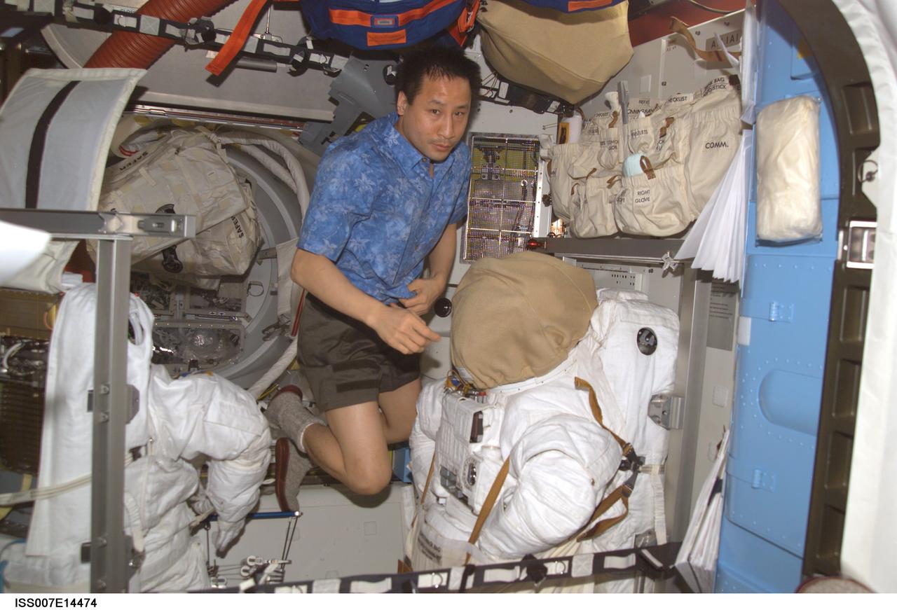 ISS007-E-14474 (5 September 2003) --- Astronaut Edward T. Lu, Expedition 7 NASA ISS science officer and flight engineer, floats near the torso portions of the Extravehicular Mobility Unit (EMU) space suits stored in the Quest airlock on the International Space Station (ISS).