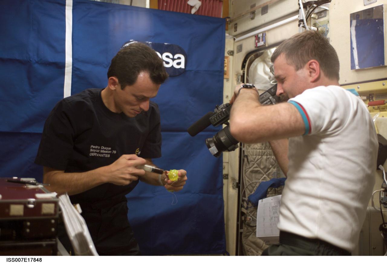 ISS007-E-17848 (23 October 2003) --- Cosmonaut Alexander Y. Kaleri (right), Expedition 8 flight engineer, uses a camera to film a scientific experiment performed by European Space Agency (ESA) astronaut Pedro Duque of Spain in the Zvezda Service Module on the International Space Station (ISS). Kaleri represents Rosaviakosmos. Duque and Kaleri performed the European educational VIDEO-2 (VID-01) experiment, which uses the Russian DSR PD-150P digital video camcorder for recording demos of several basic physical phenomena, viz., Isaac Newton's three motion laws, with narration. [The demo made use of a sealed bag containing coffee and a syringe to fill one of two hollow balls with the brown liquid (to provide "mass", as opposed to the other, "mass-less" ball).]