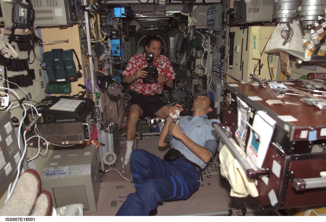 ISS007-E-18001 (25 October 2003) --- Astronaut Edward T. Lu (with camera), Expedition 7 NASA ISS science officer and flight engineer, and European Space Agency (ESA) astronaut Pedro Duque of Spain observe a bubble of liquid floating freely in the Zvezda Service Module on the International Space Station (ISS).