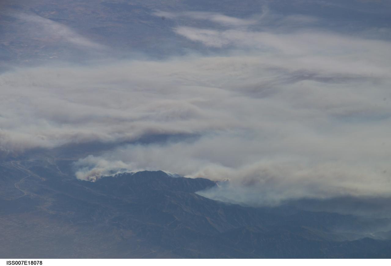 ISS007-E-18078 (26 October 2003) --- The fires in the San Bernardino Mountains, fueled by Santa Ana winds, burned out of control on the  morning of Oct. 26, 2003, when these images were taken from the International Space Station at roughly 11 a.m. (PST). Thick yellow smoke blows south, blanketing the valley below. This image and ISS007-E-18082, looking southeast, capture the smoke pall as the ISS approached and passed over the region. Image numbers 18078 and 18082 were taken roughly a minute apart. A small break in the smoke marks Cajon pass.  Content was provided by JSC&#0146;s Earth Observation Lab. The International Space Station Program {link to http://spaceflight.nasa.gov} supports the laboratory to help crew members take pictures of Earth that will be of the greatest value to scientists and the public, and to make those images freely available on the Internet. Additional images taken by astronauts and cosmonauts can be viewed at the NASA/JSC Gateway to Astronaut Photography of Earth [link to http://eol.jsc.nasa.gov/].