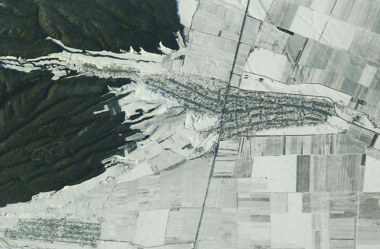 ISS008-E-09603 (20 December 2003) --- The village of Argudan near the north slopes of the Greater Caucasus Mountains in Russia is featured in this photo taken by an Expedition 8 crewmember onboard the International Space Station (ISS). The striking land use pattern, seen through a high magnification lens and highlighted by winter snow and low sun angles, produces this unique view. This rural, agricultural community sits astride the main highway about 15 kilometers east-southeast of the city of Nalchik. Shadows from a line of trees planted as a windbreak near the highway give the road a ragged appearance. A small stream flowing northeastward exits heavily forested foothills through the village and fields of intensely cultivated croplands on the plains. Snow falls through the vegetation, making the woodlands appear extremely dark compared to the snow-covered fields.