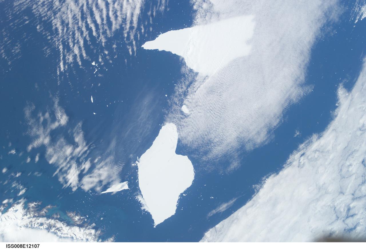 ISS008-E-12107 (6 January 2004) --- Five year old icebergs near South Georgia Island are featured in this image photographed by an Expedition 8 crewmember onboard the International Space Station (ISS). This photo shows two pieces of a massive iceberg that broke off from the Antarctica Ronne Ice Shelf in October 1998. The pieces of iceberg A-38 have floated relatively close to South Georgia Island. After five years and 3 months, they are approximately 1500 nautical miles from their origin.