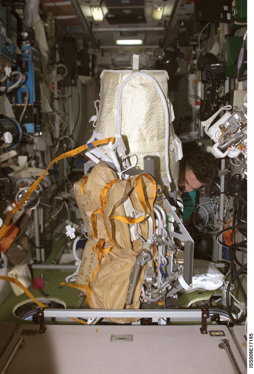 ISS008-E-17185 (24 February 2004) --- Cosmonaut Alexander Y. Kaleri, Expedition 8 flight engineer, works with the extravehicular activity (EVA) bundle in the Zvezda Service Module on the International Space Station (ISS). The Matroshka experiment package is shrouded (aft) with the brown carry bags for the CKK hardware (fwd) along with tools and other needed items. It is all bundled to a Russian EVA integrated equipment carrier. Kaleri represents Rosaviakosmos.