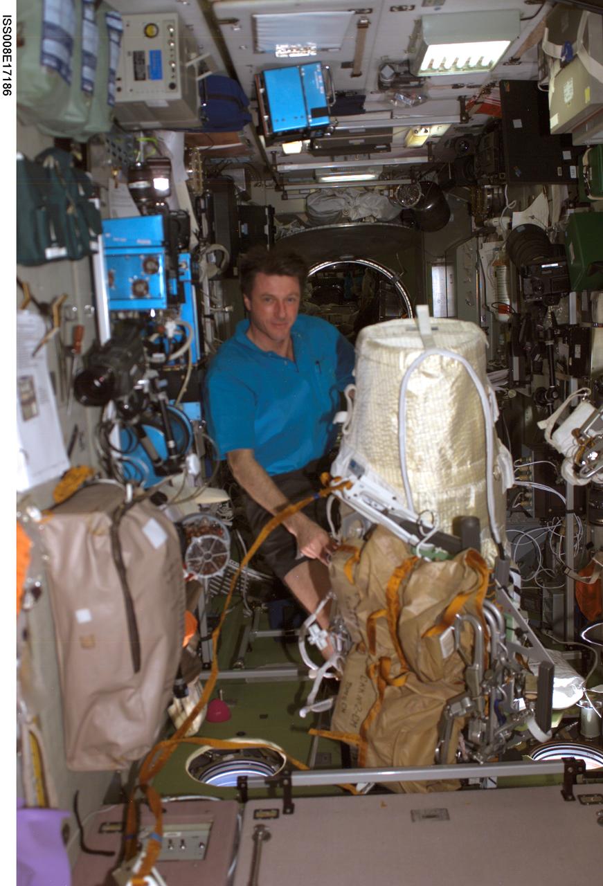 ISS008-E-17186 (24 February 2004) --- Astronaut C. Michael Foale, Expedition 8 NASA ISS science officer and commander, works with the extravehicular activity (EVA) bundle in the Zvezda Service Module on the International Space Station (ISS). The Matroshka experiment package is shrouded (aft) with the brown carry bags for the CKK hardware (fwd) along with tools and other needed items. It is all bundled to a Russian EVA integrated equipment carrier.