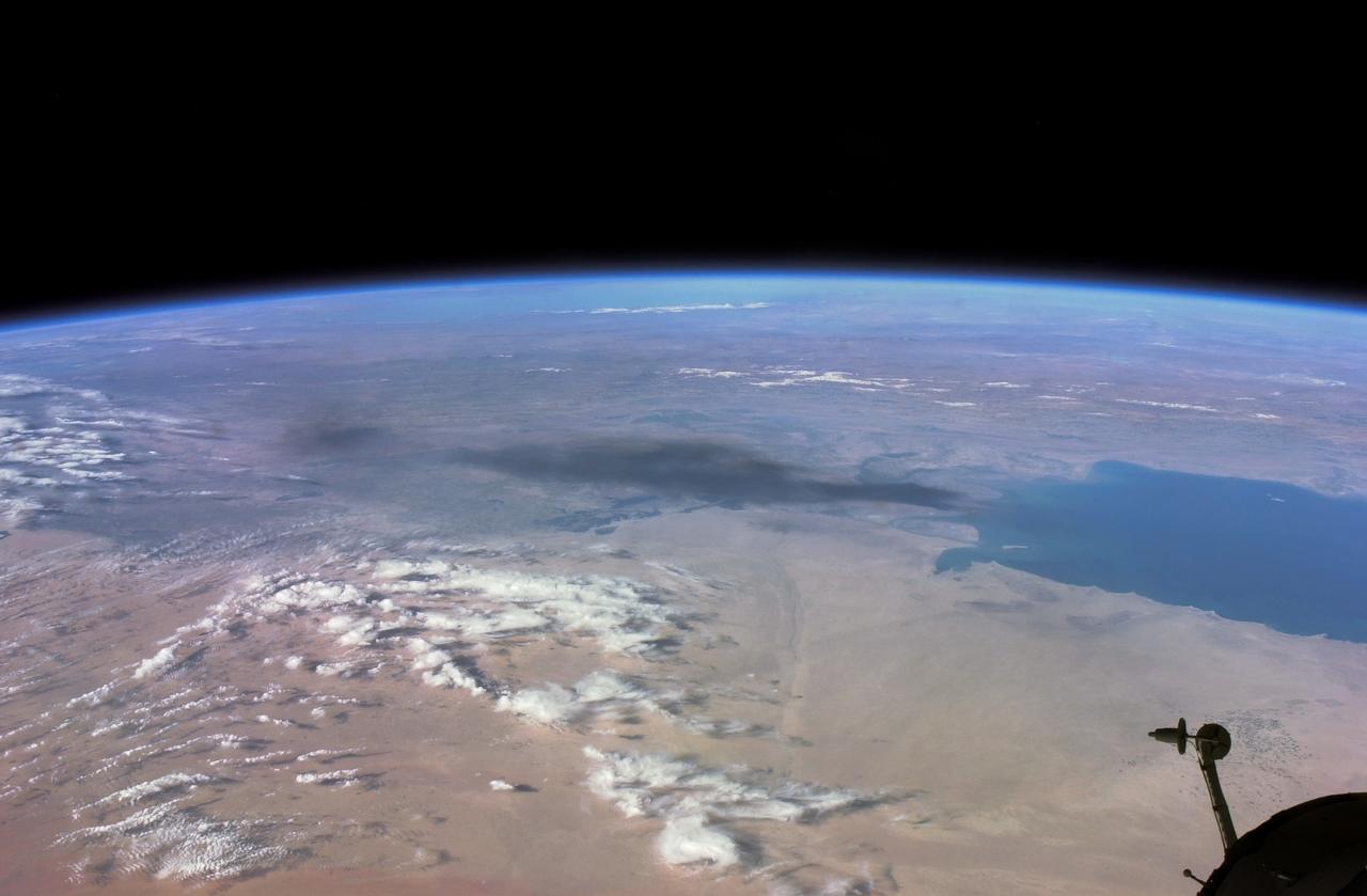 ISS008-E-18935 (24 March 2004) --- This photo of a large black smoke plume from an oil fire was taken by an Expedition 8 crewmember on the International Space Station as the Station orbited northeastward across Saudi Arabia. According to a front-page story in the New York Times, an oil pipeline near the channel of Shatt al Arab in southeastern Iraq on the Persian Gulf ruptured the day before. The resulting oil spill ignited and its smoke can here be seen to extend over 100 miles northwestward into southern Iraq.