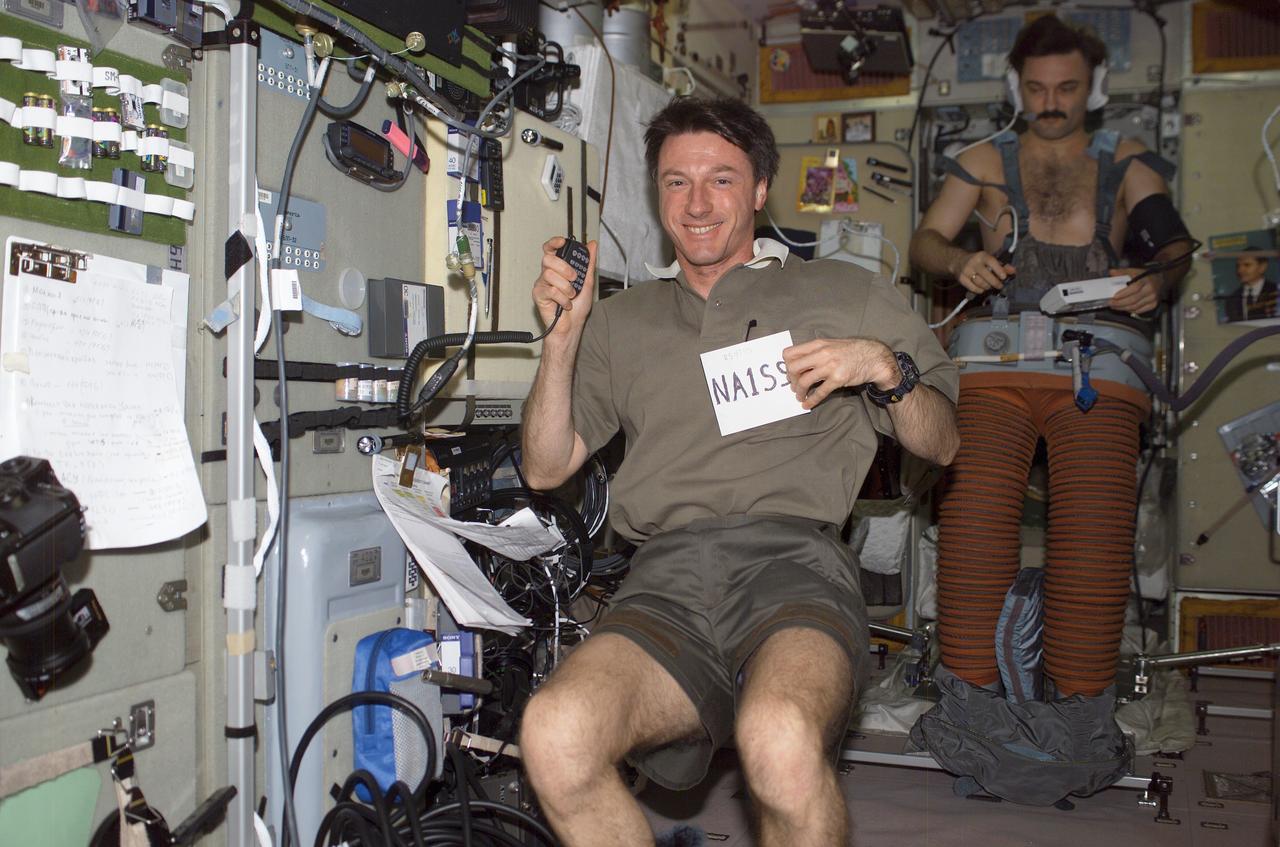 ISS008-E-21904 (April 2004) --- Astronaut C. Michael Foale, Expedition 8 commander and NASA ISS science officer, holds a portable microphone/keypad for the ARISS ham radio in one hand, and a note card with his call sign of NA1SS in the other in the Zvezda Service Module on the International Space Station (ISS). Cosmonaut Alexander Y. Kaleri, flight engineer representing Russia&#0146;s Federal Space Agency, donned in the Russian Lower Body Negative Pressure (LBNP) or Chibis suit in preparation for a return to gravity following his stay onboard the ISS, is visible in the background.