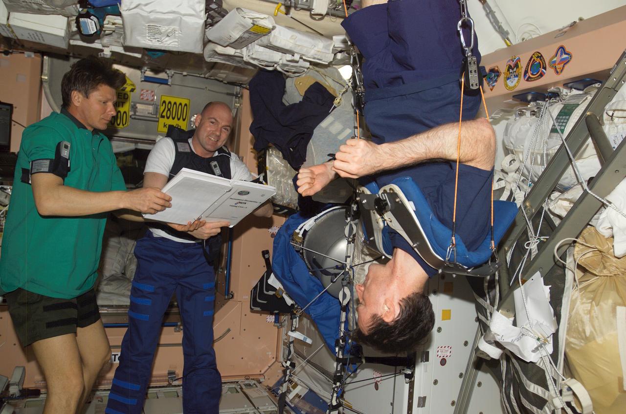 ISS008-E-21992 (22 April 2004) --- Cosmonaut Gennady I. Padalka (left), Expedition 9 commander, and European Space Agency (ESA) astronaut Andre Kuipers of the Netherlands, look over a procedures checklist for the Dutch Expedition for Life Science, Technology and Atmospheric (DELTA) Research in the Unity node of the International Space Station (ISS). Astronaut C. Michael Foale (right), Expedition 8 commander and NASA ISS science officer, exercises using the Interim Resistive Exercise Device (IRED) equipment. Padalka represents Russia’s Federal Space Agency.