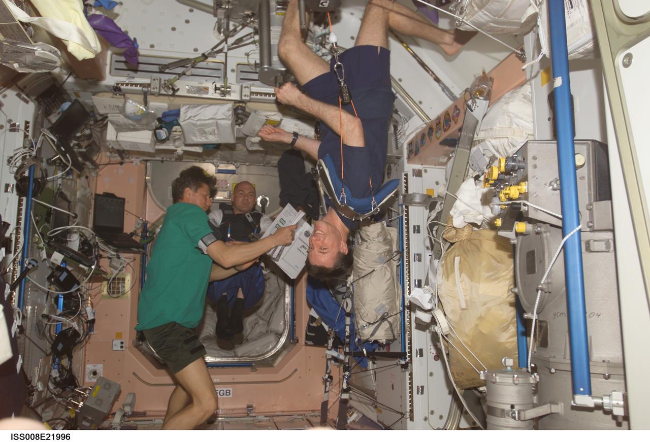 ISS008-E-21996 (22 April 2004) --- Cosmonaut Gennady I. Padalka (left), Expedition 9 commander, and European Space Agency (ESA) astronaut Andre Kuipers of the Netherlands, look over a procedures checklist for the Dutch Expedition for Life Science, Technology and Atmospheric (DELTA) Research in the Unity node of the International Space Station (ISS). Astronaut C. Michael Foale (right), Expedition 8 commander and NASA ISS science officer, exercises using the Interim Resistive Exercise Device (IRED) equipment. Padalka represents Russia’s Federal Space Agency.