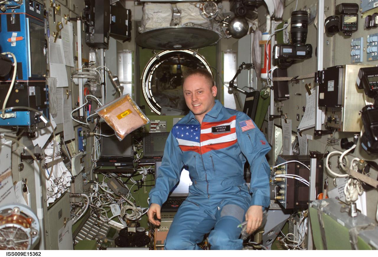 ISS009-E-15362 (17 July 2004) --- Astronaut Edward M. (Mike) Fincke, Expedition 9 NASA ISS science officer and flight engineer, is pictured in the Zvezda Service Module of the International Space Station (ISS).   A bag of tomato seeds for the Tomatosphere II Project,  an educational program sponsored by Canadian Space Agency (CSA), floats nearby. The seeds will be distributed to classrooms in Canada for use in plant growth experiments.