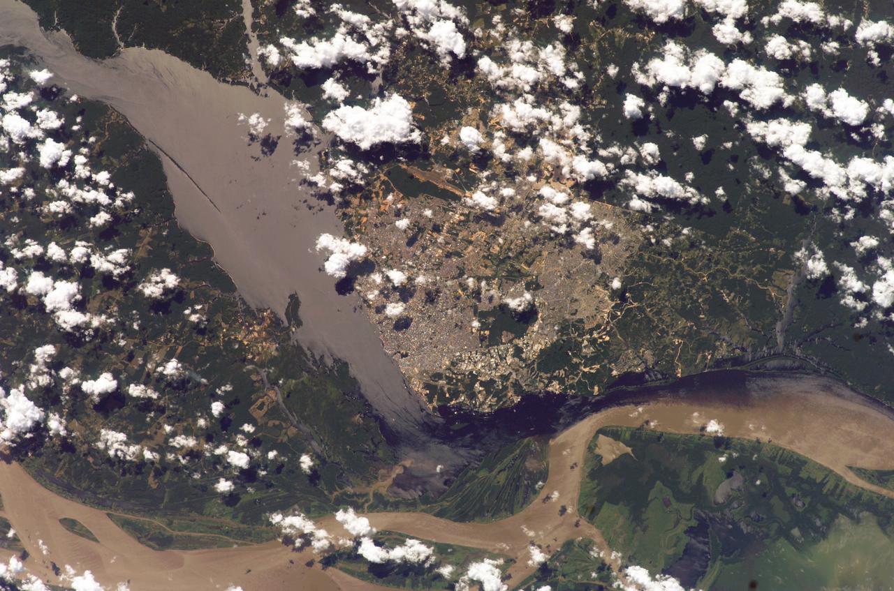 ISS009-E-15488 (7 July 2004) --- Solimoes-Negro River confluence at Manaus, Amazonia is featured in this image photographed by an Expedition 9 crewmember on the International Space Station (ISS). The largest river on the planet, the Amazon, forms from the confluence of the Solimoes (the upper Amazon River) and the Negro at the Brazilian city of Manaus in central Amazonas. At the river conjunction, the muddy, tan colored waters of the Solimoes meet the “black” water of the Negro River. The unique mixing zone where the waters meet extends downstream through the rainforest for hundreds of kilometers, and is a famous attraction for tourists all over the world. It is the vast quantity of sediment eroded from the Andes Mountains that gives the Solimoes its tan color. By comparison, water in the Negro derives from the low jungles where reduced physical erosion of rock precludes mud entering the river. In place of sediment, organic matter from the forest floor stains the river the color of black tea.