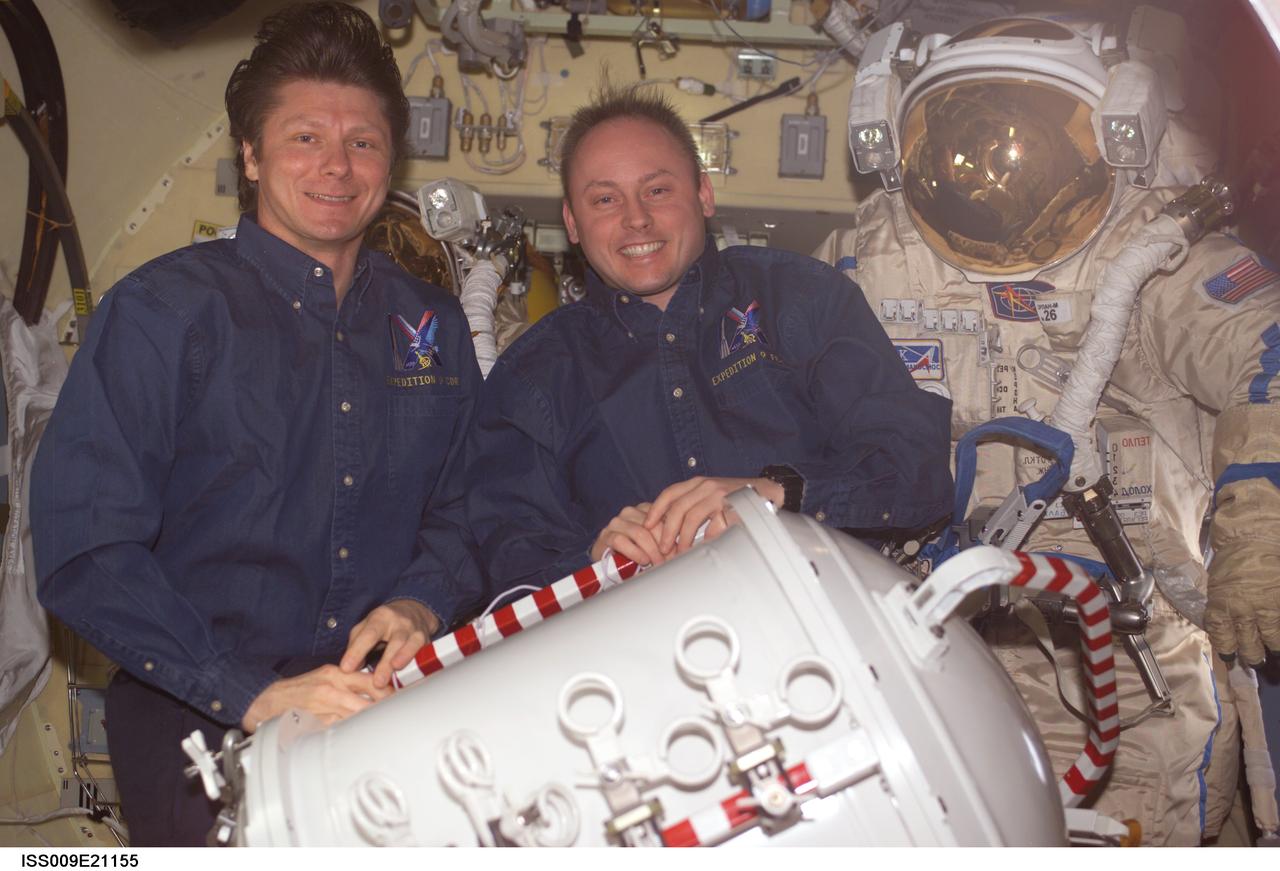 ISS009-E-21155 (1 September 2004) --- Cosmonaut Gennady I. Padalka (left), Expedition 9 commander representing Russia&#0146;s Federal Space Agency, and astronaut Edward M. (Mike) Fincke, NASA ISS science officer and flight engineer, pose with their Russian Orlan spacesuits in the Pirs Docking Compartment of the International Space Station (ISS). The container for the pump panel is in the foreground.