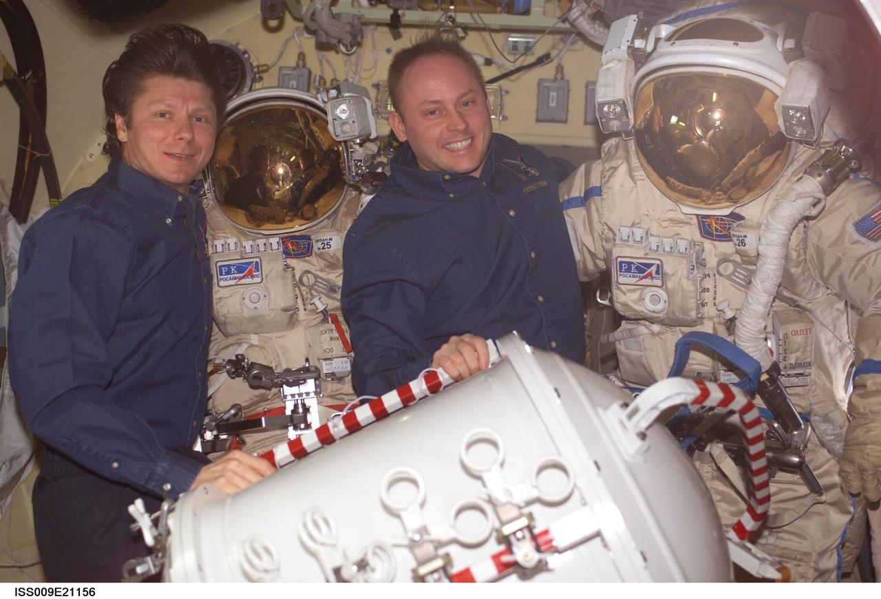ISS009-E-21156 (1 September 2004) --- Cosmonaut Gennady I. Padalka (left), Expedition 9 commander representing Russia&#0146;s Federal Space Agency, and astronaut Edward M. (Mike) Fincke, NASA ISS science officer and flight engineer, pose with their Russian Orlan spacesuits in the Pirs Docking Compartment of the International Space Station (ISS). The container for the pump panel is in the foreground.