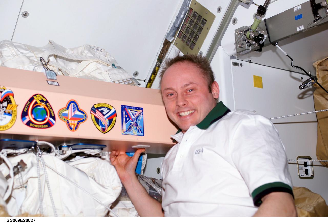 ISS009-E-28627 (1 July 2004) --- Astronaut Edward M. (Mike) Fincke, Expedition 9 NASA ISS science officer and flight engineer, poses by the Expedition mission insignias placed in the Unity node of the International Space Station (ISS).