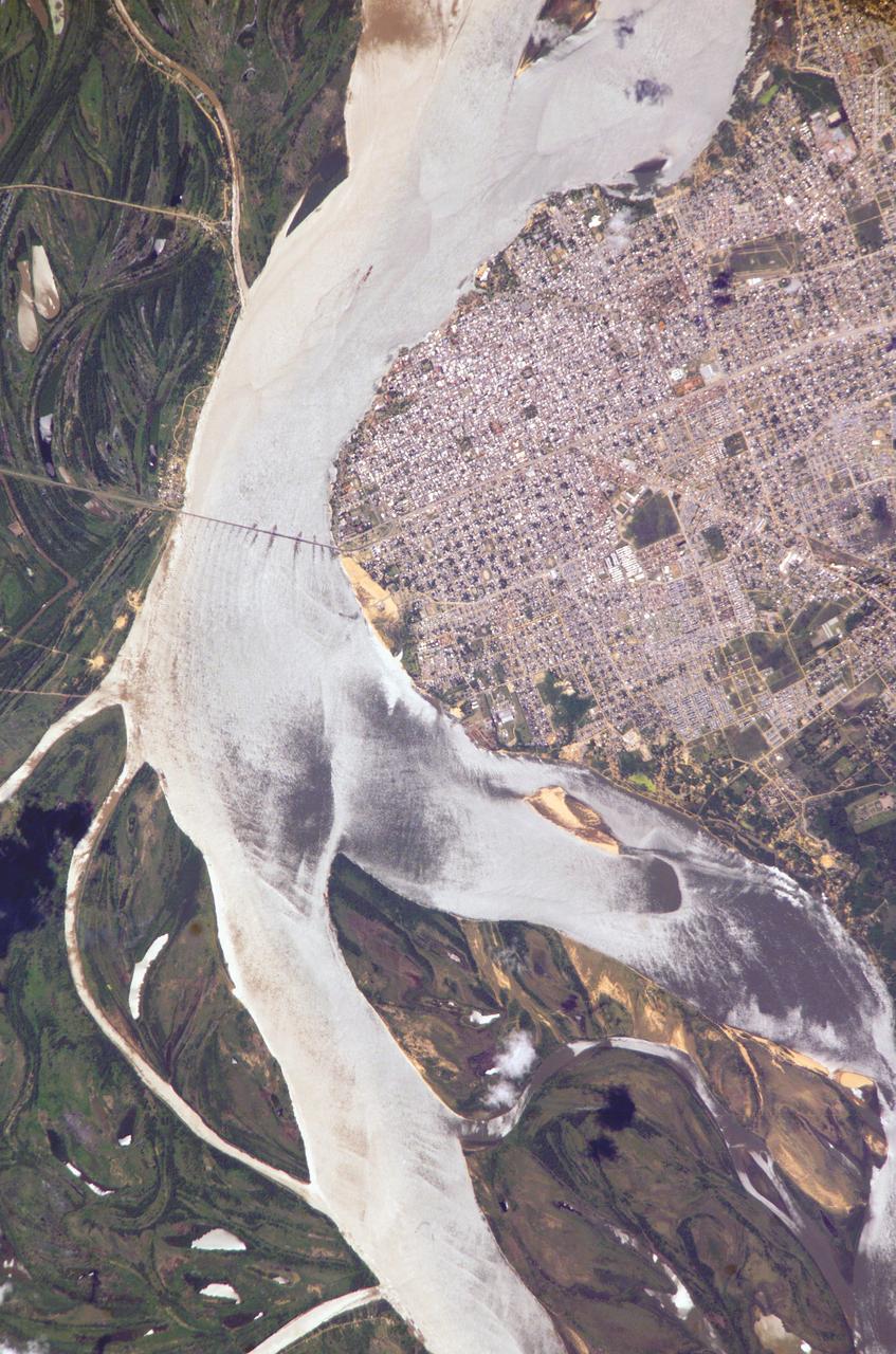 ISS010-E-05070 (25 October 2004) --- Corrientes, Argentina, and the Parana River are featured in this image photographed by an Expedition 10 crewmember on the International Space Station (ISS). Corrientes, Argentina sits on the east bank of the Parana River, South America&#0146;s third largest river (after the Negro and Amazon Rivers). From its headwaters in southeastern Brazil, the river flows southwestward around southern Paraguay, and then into Argentina. Corrientes is located just inside Argentina, across the river from the southwestern tip of Paraguay. The bridge over the Parana, built in the 1970s, connects Corrientes to its sister city, Resistencia, (beyond the left edge of image) on the western bank of the river. Sun glint on the river gives it a silvery glow and emphasizes channel islands in the river, side channels, and meander scars on the floodplain opposite the city, and even reveals the pattern of disturbed flow downstream of the bridge pylons. The old part of the city appears as a zone of smaller, more densely clustered city blocks along the river to the north of a major highway, which runs through Corrientes from the General Belgrano Bridge to the northeast (upper right of image). Larger blocks of the younger cityscape, with more green space, surround these core neighborhoods.