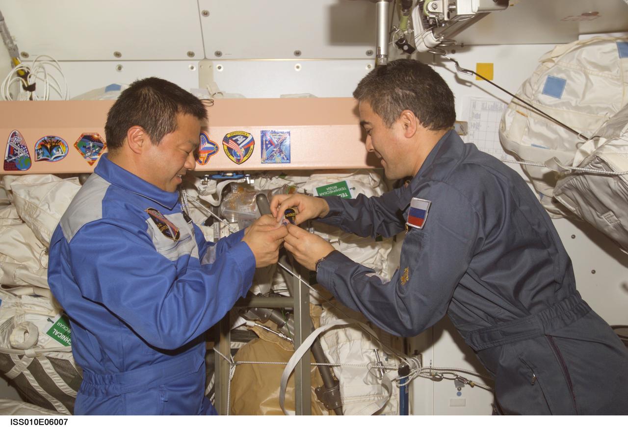 ISS010-E-06007 (6 November 2004) --- Astronaut Leroy Chiao (left), Expedition 10 commander and NASA ISS science officer, and cosmonaut Salizhan S. Sharipov, flight engineer representing Russia's Federal Space Agency, add their crew&#0146;s patch to the Unity node&#0146;s growing collection of insignias representing crews who have worked on the International Space Station (ISS).