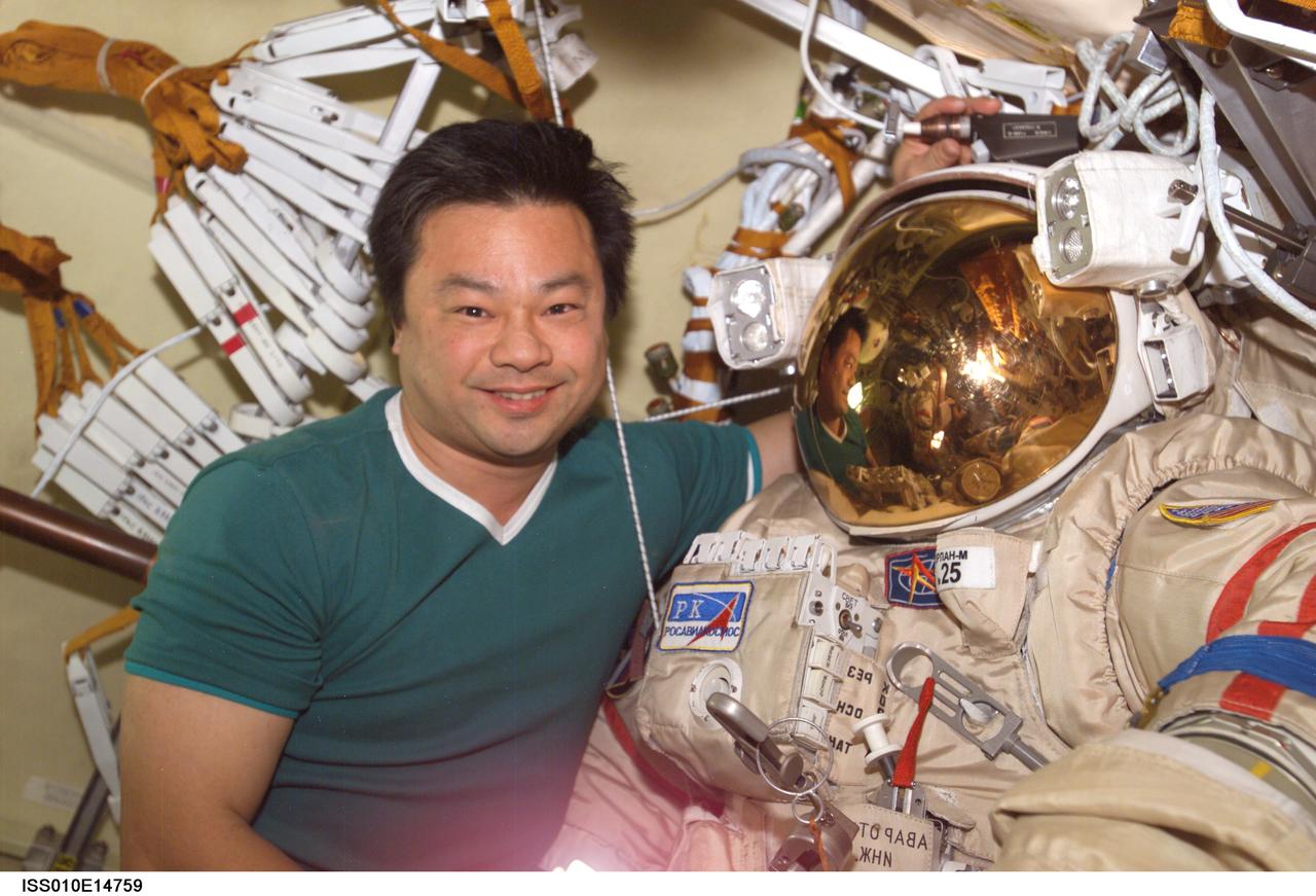 ISS010-E-14759 (24 January 2005) --- Astronaut Leroy Chiao, Expedition 10 commander and NASA ISS science officer, poses with his Russian Orlan spacesuit in the Pirs Docking Compartment of the International Space Station (ISS). Chiao and cosmonaut Salizhan S. Sharipov (out of frame), flight engineer representing Russia's Federal Space Agency, were conducting extravehicular activity (EVA) preparations for the spacewalk scheduled for January 26.