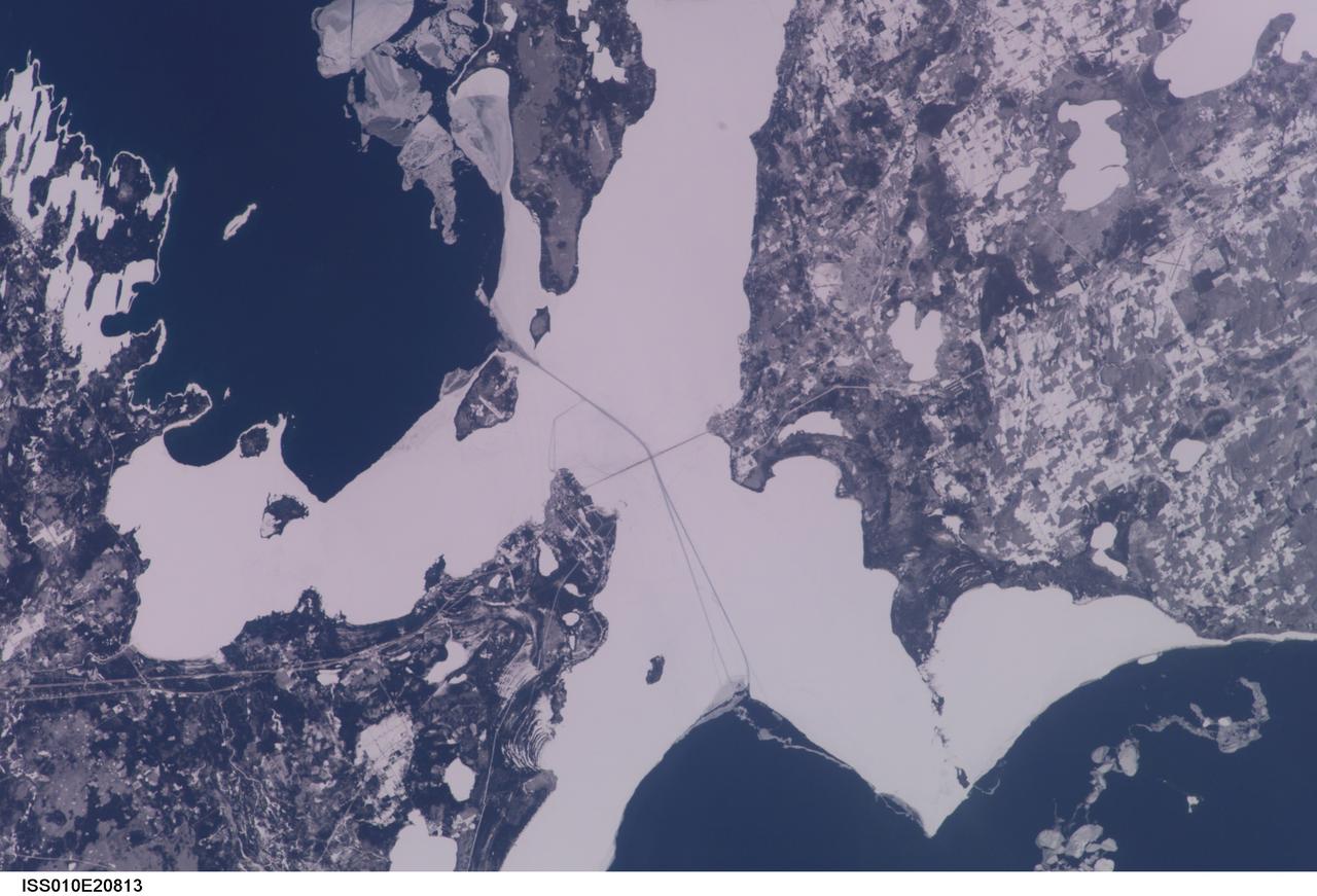 ISS010-E-20813 (22 March 2005) --- The Straits of Mackinac are featured in this image photographed by an Expedition 10 crewmember on the International Space Station (ISS). The Mackinac Bridge spans a stretch of water five miles wide between Michigan&#0146;s lower and upper peninsulas. The strait connects Lakes Michigan (left) and Huron (right). The bridge is a combination of pier-supported spans with a high, central suspension sector that allows passage of lake steamers. The suspension sector is the longest in the Americas (8614 feet or 1.6 miles). Prior to construction of the bridge, the only passage across the straits was by ferryboat. This view shows shipping lanes opened by ice breakers.  A narrow passage leads to the small town of St. Ignace at the north end of the bridge (Mackinaw City appears at the south end). The shipping channel is maintained even through remnants of the ice mass, but the ice ridges can be hazardous to shipping during ice break-up.