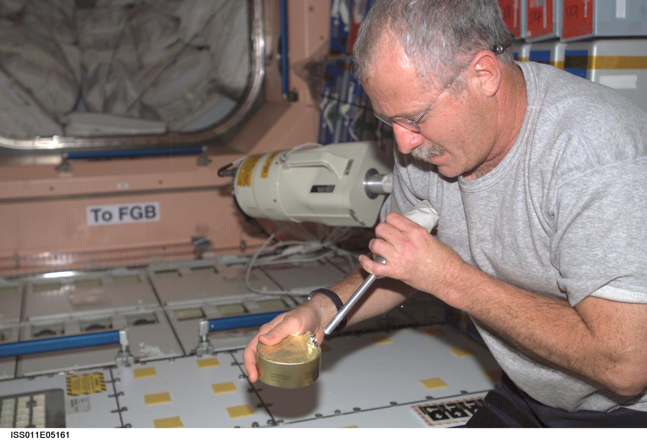 ISS011-E-05161 (17 April 2005) --- Astronaut John L. Phillips, Expedition 11 NASA ISS science officer and flight engineer, uses the ISS wet/dry vacuum cleaner assembly to catch floating debris from the top of a food can in the Unity node of the International Space Station (ISS).