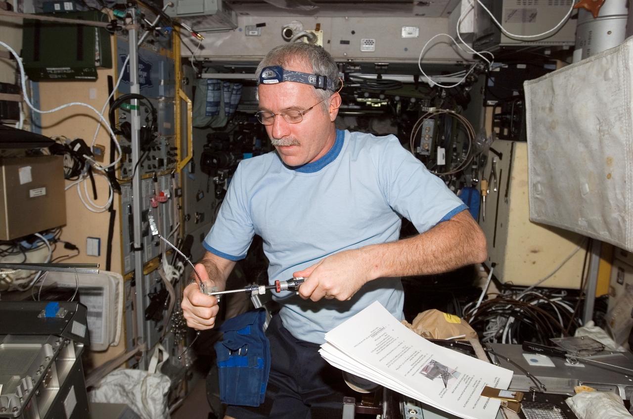 ISS011-E-06174 (16 May 2005) --- Astronaut John L. Phillips, Expedition 11 NASA science officer and flight engineer, works with the Treadmill Vibration Isolation System (TVIS) during In-Flight Maintenance (IFM) in the Zvezda Service Module of international space station. Phillips uses a screwdriver to repair one of the broken forward and aft gyroscope wire ropes.
