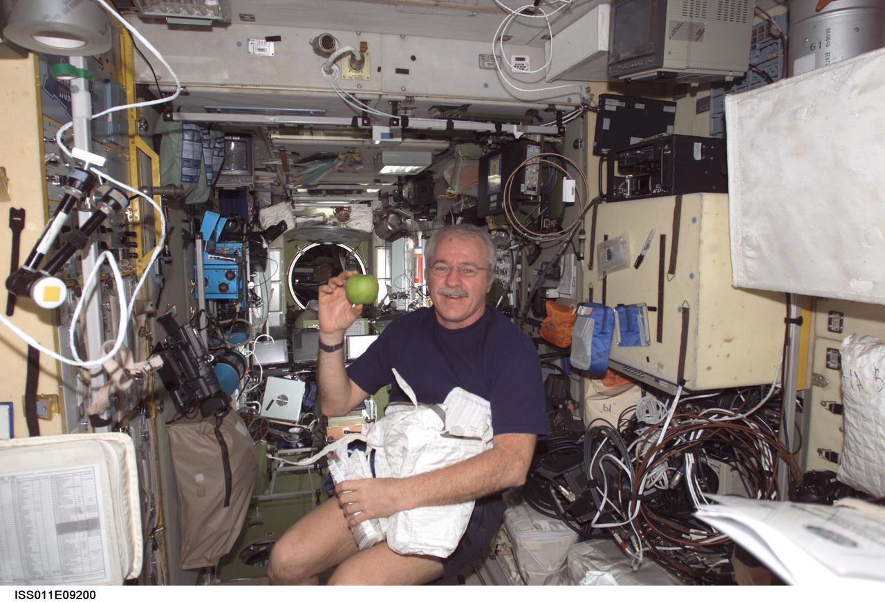 ISS011-E-09200 (19 June 2005) --- Astronaut John L. Phillips, Expedition 11 NASA space station science officer and flight engineer, holds small packages of supplies and fruit in the Zvezda Service Module of the International Space Station, which he un-stowed from the docked Progress 18 supply vehicle.