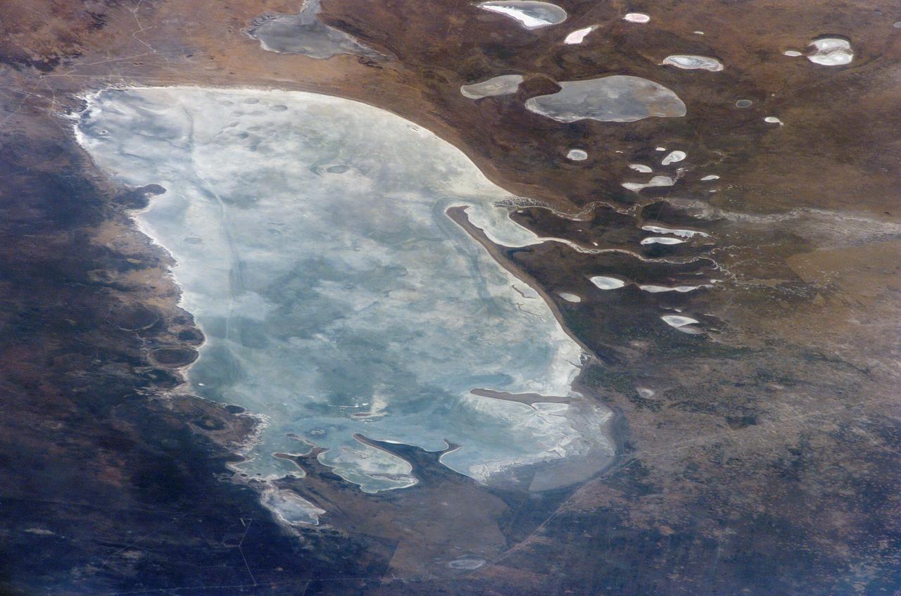 ISS011-E-09504 (24 June 2005) --- Ekuma River and Etosha Pan, Namibia are featured in this image photographed by an Expedition 11 crewmember on the International Space Station. Etosha Pan, northern Namibia, is a large (120 kilometers or 75 mile long) dry lakebed in the Kalahari Desert. The lake and surrounds are protected today as one of Namibia&#0146;s largest wildlife parks. Herds of elephants occupy the dense mopane woodland on the south side of the lake. Mopane trees are common throughout south-central Africa, and host the mopane worm (the larval form of the Mopane Emperor Moth)&#0150;an important source of protein for rural communities. According to scientists, about 16,000 years ago, when ice sheets were melting across Northern Hemisphere land masses, a wet climate phase in southern Africa filled Etosha Lake. Today, Etosha Pan is seldom seen with even a thin sheet of water covering the salt pan. Typically, little river water or sediment reaches the dry lake because water seeps into the riverbed along its 250 kilometers (155 miles) course, reducing discharge along the way.