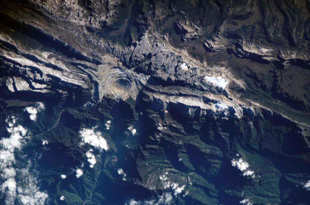 ISS011-E-09620 (26 June 2005) --- Grasberg Mine, Indonesia is featured in this image photographed by an Expedition 11 crewmember on the International Space Station. Located in the Sudirman Mountains of the Irian Jaya province of Indonesia, the Grasberg complex (also known as the Freeport Mine) is one of the largest gold and copper mining operations in the world. The Sudirman Mountains form the western portion of the Maoke Range that extend across Irian Jaya from west to the east-southeast. According to scientists, these ranges were formed by ongoing collision of the northward-moving Australian and westward-moving Pacific tectonic plates. Intrusion of hot magma into sedimentary rock layers during uplift of the mountains resulted in the formation of copper- and gold-bearing ore bodies. Rich copper ore bodies were discovered in the area in 1936, and the Grasberg gold-bearing ore bodies were discovered in 1988. This image illustrates the approximately 4 kilometers-wide open-pit portion of the mine complex; there are also extensive underground mine workings. Access roads for trucks hauling ore and waste rock are visible along the sides of the pit.