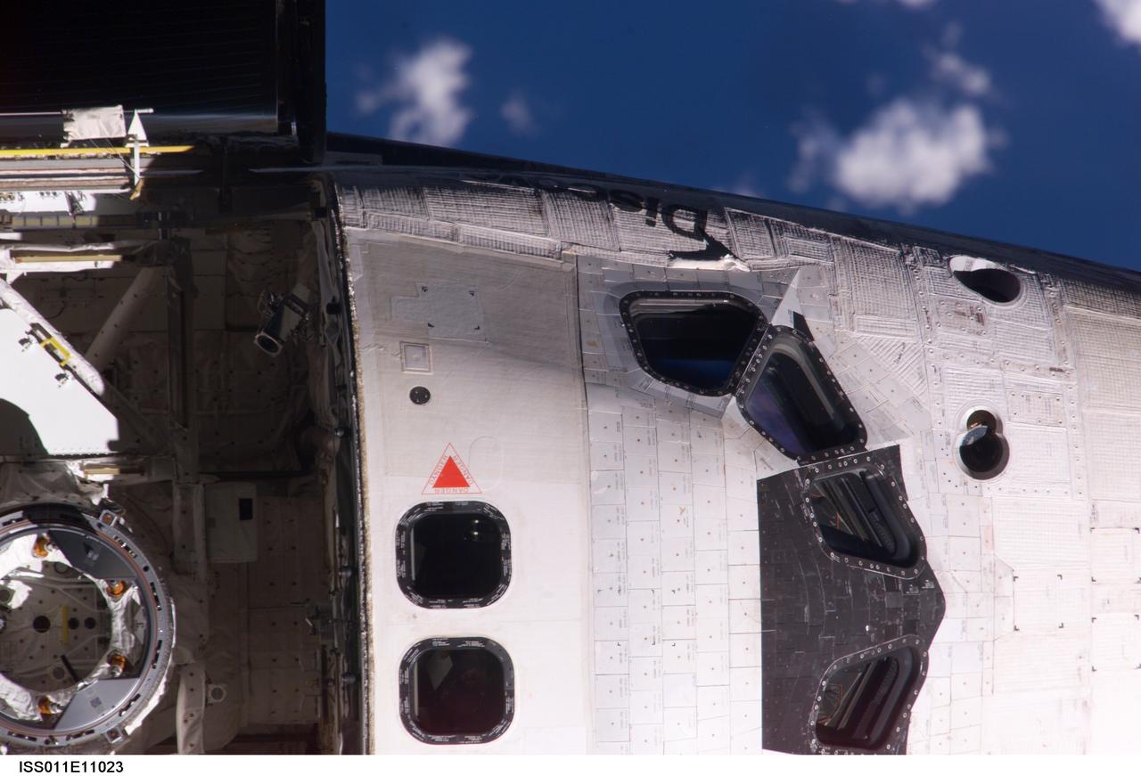 ISS011-E-11023 (28 July 2005) --- View of the Space Shuttle Discovery's crew cabin and the Orbiter Docking System (ODS), photographed as part of  the survey sequence performed by the Expedition 11 crew during the STS-114 R-Bar Pitch Maneuver on Flight Day 3.  This picture was used by Steve M. Poulos, Jr.  Manager, Space Shuttle Vehicle Engineering Office, as one of his visual aids in a July 28, 2005 press conference in the Teague Auditorium at the Johnson Space Center. Poulos pointed out a raised area of thermal blanket material just below a window on the commander's (port) side of the cabin.
