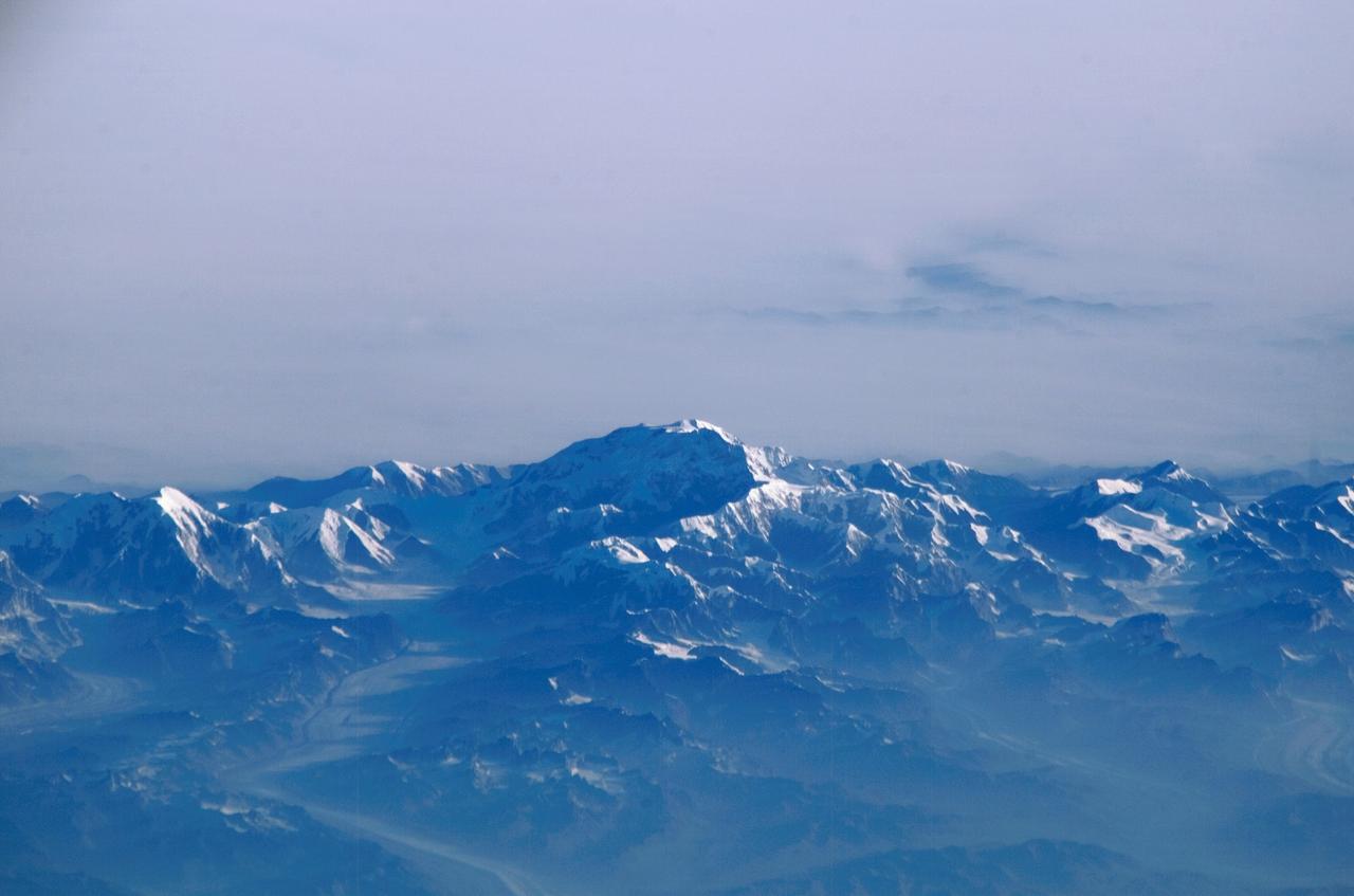 ISS011-E-11806 (14 August 2005) --- Mount McKinley, Alaska is featured in this image photographed by an Expedition 11 crewmember on the international space station. This view &#0150; of the highest point in North America (20,230 feet) looks as if it were taken from an aircraft. The station crewmember took advantage of cloud free skies and the powerful 800 mm lens to photograph this peak, fully 800 miles to the north of the spacecraft, which was located over the Gulf of Alaska. The powerful lenses are difficult to use, requiring motion compensation by the astronaut, so that these kinds of detailed images of horizon detail are seldom taken. The rising sun casts long shadows across the Kahiltna Glacier that angles down from Mt. McKinley (lower left). Other glaciers with moraine lines appear at far left and far right. Despite the blueness inherent in images taken at great distance, this image also shows unusually dense atmospheric haze at lower altitudes: all the valleys in the foreground appear murky due to forest fire smoke.