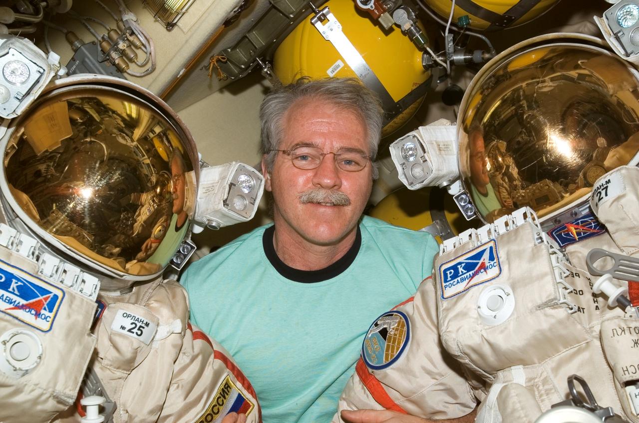 ISS011-E-11983 (17 August 2005) --- Astronaut John L. Phillips, Expedition 11 NASA science officer and flight engineer, poses with Russian Orlan spacesuits in the Pirs Docking Compartment of the international space station. The mission&#0146;s first spacewalk is scheduled for August 18.