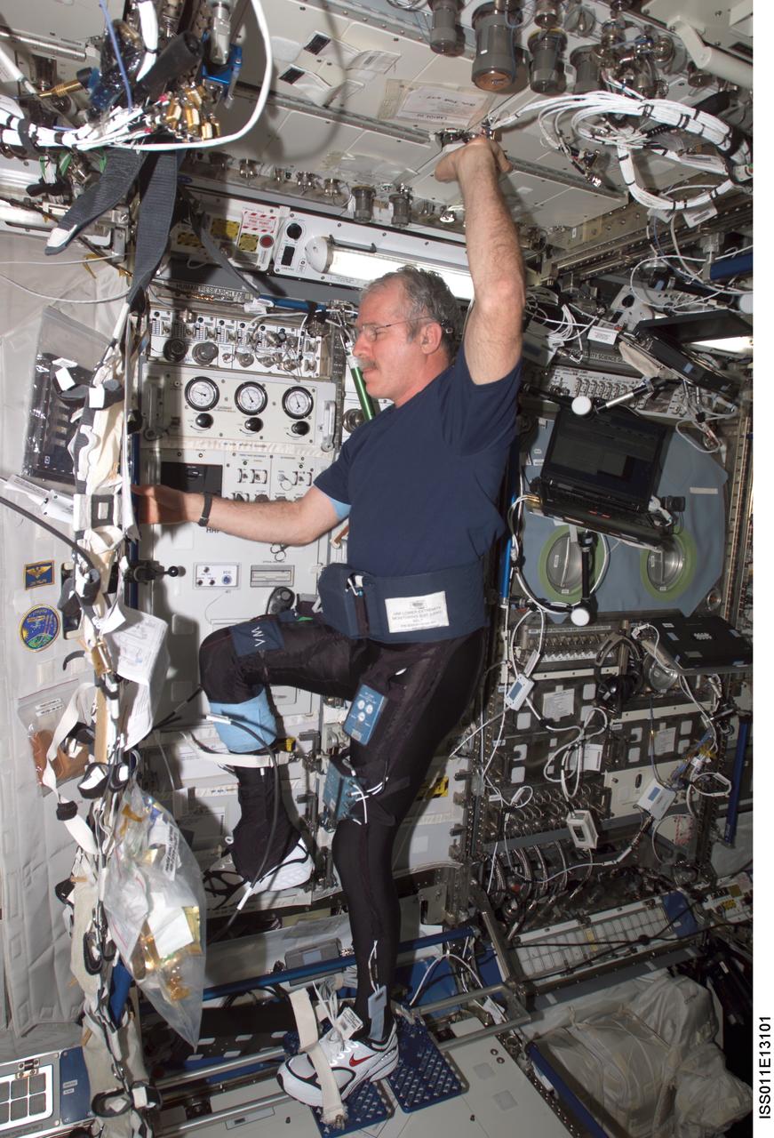ISS011-E-13101 (16 Sept. 2005) --- Astronaut John L. Phillips, Expedition 11 NASA space station science officer and flight engineer, balances on the footplate of a special track attached to the Human Research Facility (HRF) rack in the Destiny laboratory on the International Space Station to perform Foot/Ground Reaction Forces During Spaceflight (FOOT) / Electromyography (EMG) calibration operations. Phillips is wearing the Lower Extremity Monitoring Suit (LEMS), the cycling tights outfitted with 20 sensors, which measures forces on joints and muscle activity.