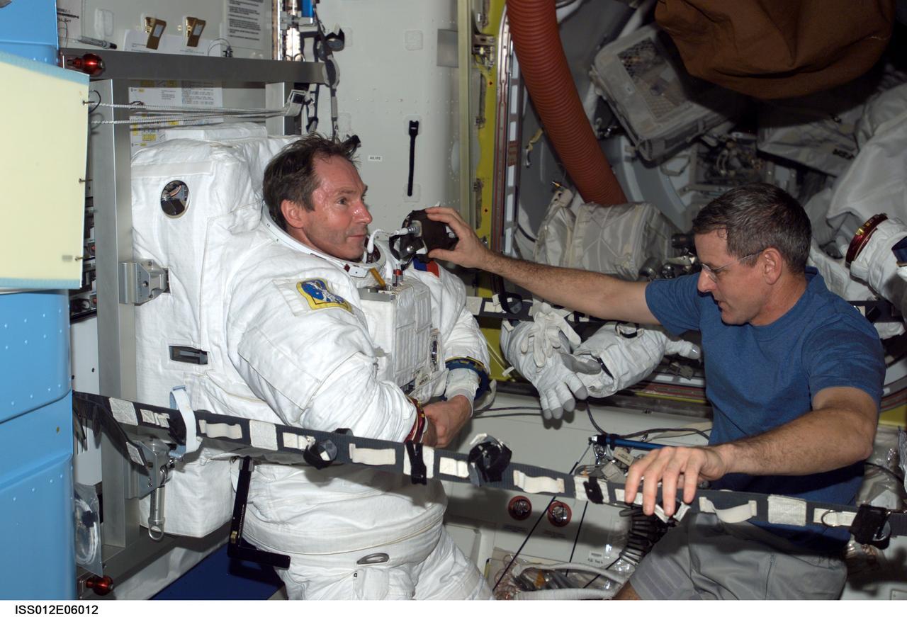 ISS012-E-06012 (23 October 2005) --- Cosmonaut Valery I. Tokarev (left), Expedition 12 flight engineer representing Russia's Federal Space Agency, dons his Extravehicular Mobility Unit (EMU) spacesuit in the Quest Airlock of the international space station. Astronaut William S. McArthur Jr., commander and NASA science officer, assisted Tokarev. When the Expedition 12 crew performs its first scheduled day of spacewalking on Nov. 7, it will be attired in the NASA EMU.