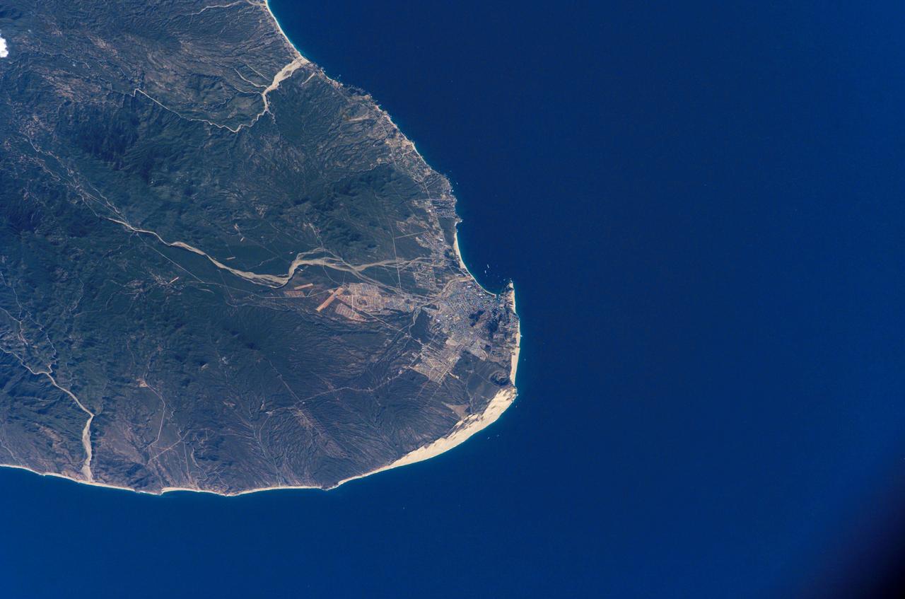 ISS012-E-07151 (5 November 2005) --- Cabo San Lucas, Baja California Sur, Mexico is featured in this image photographed by an Expedition 12 crewmember on the International Space Station. The built-up areas of the Cabo (cape) San Lucas stand out as bright, angular areas inland from the main bay on the tip of the Baja California peninsula. The town is centered on the bay, which looks out onto the blue waters of the Gulf of California. Three dry river beds (white sands in this arid environment) descend from rugged, wooded hills to the coastline. Rivers sands then accumulate to form white beaches visible along the coastline adjacent to the city. Cabo San Lucas (current population 41,000) is a tourist hotspot known for its mild sunny winter weather, and is frequented mainly by visitors from around the world. New neighborhoods are spreading north and northwest along major roads, and larger developments stretch northeast along the coast for 40 kilometers from Cabo San Lucas to the slightly larger city of San Jose del Cabo (not visible).