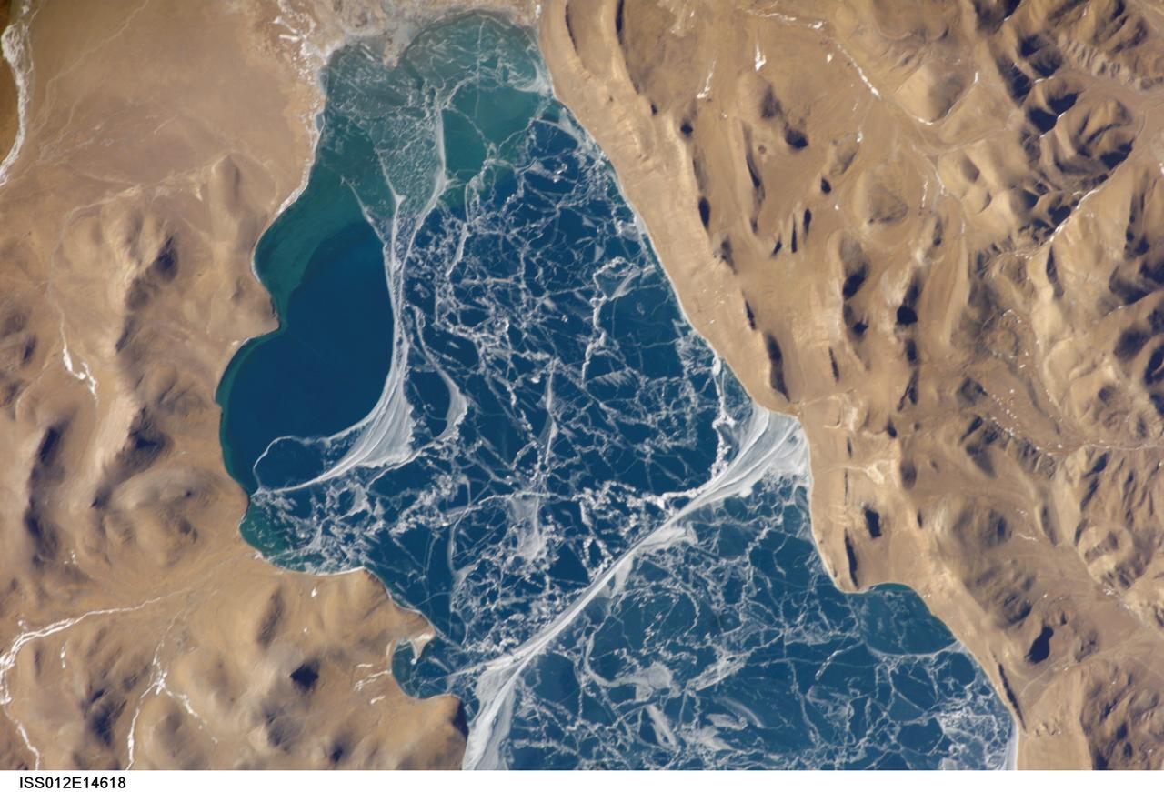 ISS012-E-14618 (6 Jan. 2006) --- A portion of Lake Puma Yumco and parts of Tibet and China are featured in this image photographed by an Expedition 12 crew member on the International Space Station. The alpine lakes of the Tibetan Plateau are some of the most remote in the world. This image depicts Lake Puma Yumco during the winter season. The lake is located at an elevation of 5,030 meters above sea level, and is considered ultraoligotrophic in that nutrient concentrations in both the water column and lake sediments are extremely low. Water in such lakes tends to be blue to blue-green and have high clarity due to the lack of abundant photosynthesizing organisms such as phytoplankton. Water color change in these lakes is usually due to shallowing of the water &#0150; blue indicating deeper water - as is visible in the depth transition along the west/southwestern shoreline (left). The maximum dimensions of the lake are 31 kilometers by 14 kilometers, indicating that the ice blocks range from less than ten to hundreds of meters in diameter. According to scientists, the ice pattern is caused by repeated cycles of freezing, fracturing, and refreezing of the ice due to variations in temperature and wind-induced ice motion. A prominent white linear feature extending north-south across the center of the lake (lower center) is suggestive of an ice ridge formed by east-west winds subsequently highlighted by snow.