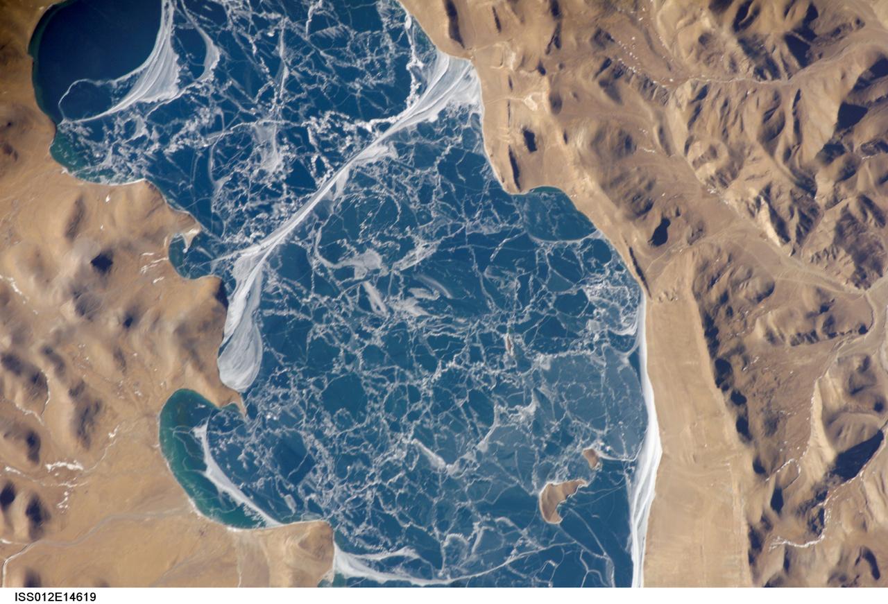 ISS012-E-14619 (6 Jan. 2006) --- A portion of Lake Puma Yumco and parts of Tibet and China are featured in this image photographed by an Expedition 12 crew member on the International Space Station. The alpine lakes of the Tibetan Plateau are some of the most remote in the world. This image depicts Lake Puma Yumco during the winter season. The lake is located at an elevation of 5,030 meters above sea level, and is considered ultraoligotrophic in that nutrient concentrations in both the water column and lake sediments are extremely low. Water in such lakes tends to be blue to blue-green and have high clarity due to the lack of abundant photosynthesizing organisms such as phytoplankton. Water color change in these lakes is usually due to shallowing of the water – blue indicating deeper water - as is visible in the depth transition along the west/southwestern shoreline (upper left). The maximum dimensions of the lake are 31 kilometers by 14 kilometers, indicating that the ice blocks range from less than ten to hundreds of meters in diameter. According to scientists, the ice pattern is caused by repeated cycles of freezing, fracturing, and refreezing of the ice due to variations in temperature and wind-induced ice motion. A prominent white linear feature across the center of the lake is suggestive of an ice ridge formed by east-west winds subsequently highlighted by snow.