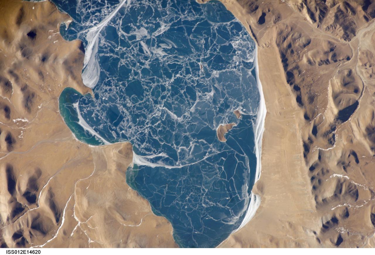 ISS012-E-14620 (6 Jan. 2006) --- A portion of Lake Puma Yumco and parts of Tibet and China are featured in this image photographed by an Expedition 12 crew member on the International Space Station. The alpine lakes of the Tibetan Plateau are some of the most remote in the world. This image depicts Lake Puma Yumco during the winter season. The lake is located at an elevation of 5,030 meters above sea level, and is considered ultraoligotrophic in that nutrient concentrations in both the water column and lake sediments are extremely low. Water in such lakes tends to be blue to blue-green and have high clarity due to the lack of abundant photosynthesizing organisms such as phytoplankton. The maximum dimensions of the lake are 31 kilometers by 14 kilometers, indicating that the ice blocks range from less than ten to hundreds of meters in diameter. According to scientists, the ice pattern is caused by repeated cycles of freezing, fracturing, and refreezing of the ice due to variations in temperature and wind-induced ice motion. A prominent white linear feature across the center of the lake (partially visible in upper left in this image) is suggestive of an ice ridge formed by east-west winds subsequently highlighted by snow.