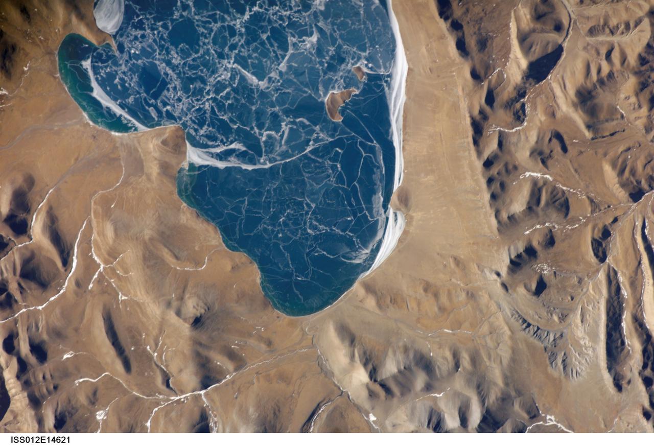 ISS012-E-14621 (6 Jan. 2006) --- A portion of Lake Puma Yumco and parts of Tibet and China are featured in this image photographed by an Expedition 12 crew member on the International Space Station. The alpine lakes of the Tibetan Plateau are some of the most remote in the world. This image depicts Lake Puma Yumco during the winter season. The lake is located at an elevation of 5,030 meters above sea level, and is considered ultraoligotrophic in that nutrient concentrations in both the water column and lake sediments are extremely low. Water in such lakes tends to be blue to blue-green and have high clarity due to the lack of abundant photosynthesizing organisms such as phytoplankton. Water color change in these lakes is usually due to shallowing of the water &#0150; blue indicating deeper water. The maximum dimensions of the lake are 31 kilometers by 14 kilometers, indicating that the ice blocks range from less than ten to hundreds of meters in diameter. According to scientists, the ice pattern is caused by repeated cycles of freezing, fracturing, and refreezing of the ice due to variations in temperature and wind-induced ice motion. A prominent white linear feature across the center of the lake (not visible in this image) is suggestive of an ice ridge formed by east-west winds subsequently highlighted by snow.