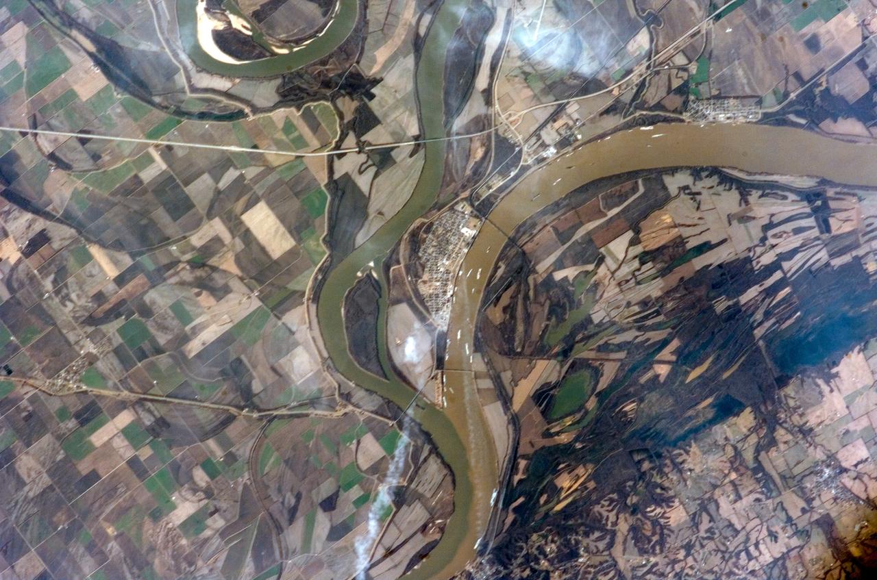 ISS012-E-15035 (12 Jan. 2006) --- The confluence of the Ohio and Mississippi Rivers at Cairo, Illinois is featured in this image photographed by an Expedition 12 crew member on the International Space Station. The Ohio River becomes a tributary of the Mississippi River directly to the south of Cairo, Illinois, a small city on the spit of land where the rivers converge (at center of image). Brown sediment-laden water flowing generally northeast to south from the Ohio River is distinct from the green and relatively sediment-poor water (northwest- to south-flowing) of the Mississippi River. The coloration of the rivers in this image is reversed from the usual condition of a green Ohio and a brown Mississippi. According to scientists, this suggests that recent precipitation in the Ohio River watershed, with very high rainfall over the Appalachians and the northeastern United States in December 2005, has led to a greater sediment load in the Ohio waters. The distinct boundary between the two river’s waters indicates that little to no mixing occurs even 3-4 miles (5-6 kilometers) downstream. The city of Cairo became a prosperous port following the Civil War due to increased riverboat and railroad commerce. Small features on the Ohio are river barges and indicate the continued importance of Cairo as a transport hub. Flooding of the Ohio and Mississippi Rivers presents a continual danger to the city; this danger is lessened by the Birds Point-New Madrid Floodway that begins directly to the south of the river confluence. The floodway lowers flood stages upstream (such as at Cairo) and adjacent to the floodway during major flood events. Part of the extensive levee system associated with flood control of the Mississippi River is visible in the image. Barlow Bottoms (image right), located in adjacent Kentucky, are a wetlands bird watching location that is replenished by periodic floods and releases of Ohio River water.