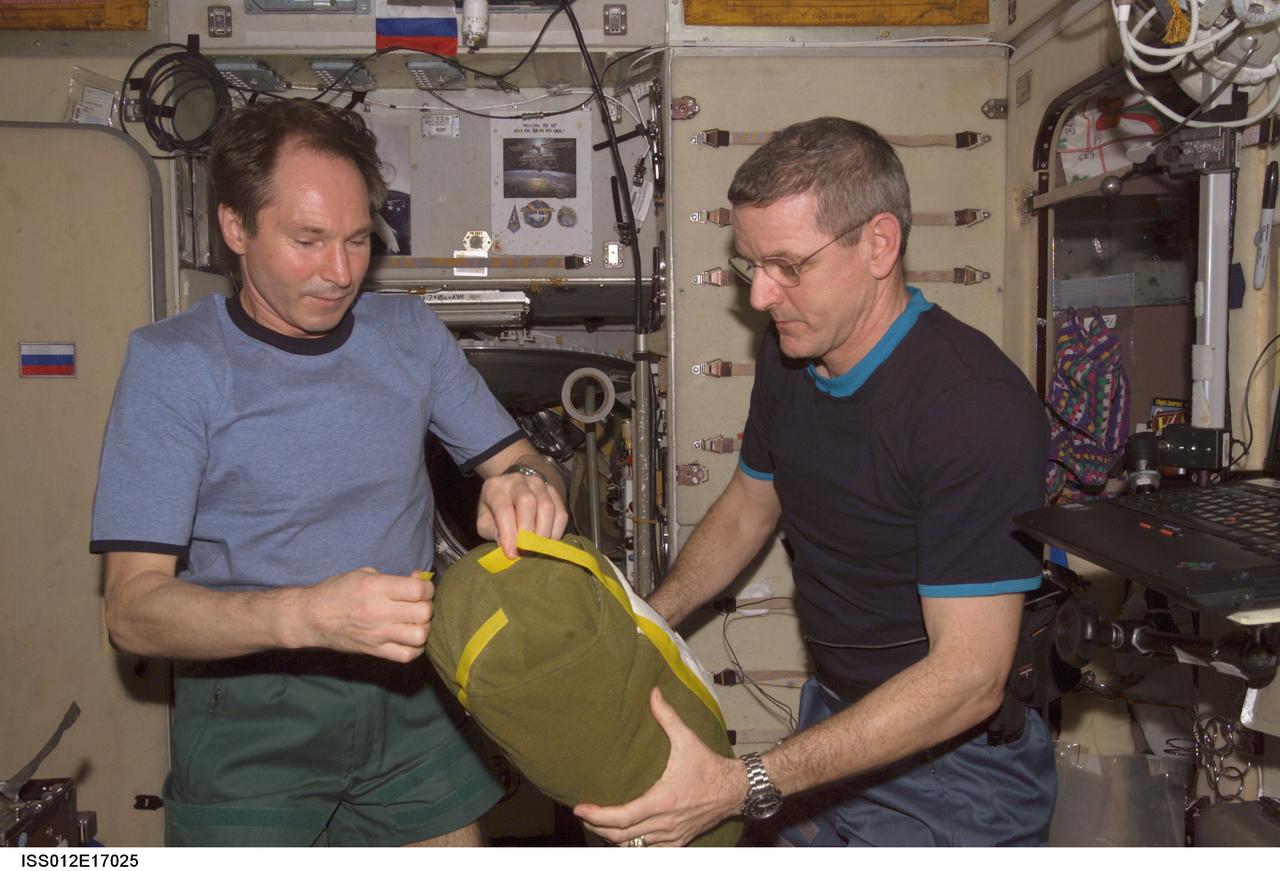 ISS012-E-17025 (23 Jan. 2006) --- Cosmonaut Valery I. Tokarev (left), Expedition 12 flight engineer representing Russia's Federal Space Agency, and astronaut William S. (Bill) McArthur, commander and NASA space station science officer, unpack the Radioskaf (SuitSat) package sent up on a Progress spacecraft. It contained instructions and a compact disk that included items such as artwork and photos from different schools.