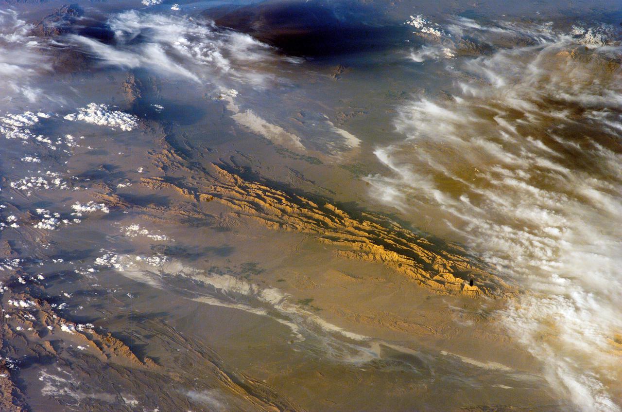 ISS012-E-18779 (28 Feb. 2006) --- Winter in the Dasht-e-Lut Desert, eastern Iran is featured in this image photographed by an Expedition 12 crew member on the International Space Station. The image takes advantage of the low angle of illumination to reveal linear geological structures of the Iranian mountain range bordering the western edge of the basin known as Dasht-e-Lut. The range rises 1818 meters (6000 feet) above sea level and lies 750 kilometers (466 miles) north of the Persian Gulf. The convoluted appearance results from erosion of folded and faulted rocks &#0150; softer rocks erode away quickly, leaving more resistant rock to form linear ridges perpendicular to the direction of compression. While not a major oil producing region like the Zagros Fold Belt to the southwest, the mountains of east-central Iran contain economically important deposits of copper and other metals. Little vegetation is visible from space in the arid interior basin of the Dasht-e-Lut. Iran is climatically part of the Afro-Asian belt of deserts that stretch from the Cape Verde islands off West Africa all the way to Mongolia near Beijing. The patchy, elongated, light-colored feature in the foreground (parallel to the mountain range) is the northernmost of the Dasht dry lakes that stretch southward 300 kilometers (186 miles). High country is the source of precipitation-derived water in all near-tropical deserts. Agricultural fields (small dark patches in the image) that depend on this precipitation are located down slope near the margin of the dry, salty soils of the lake.