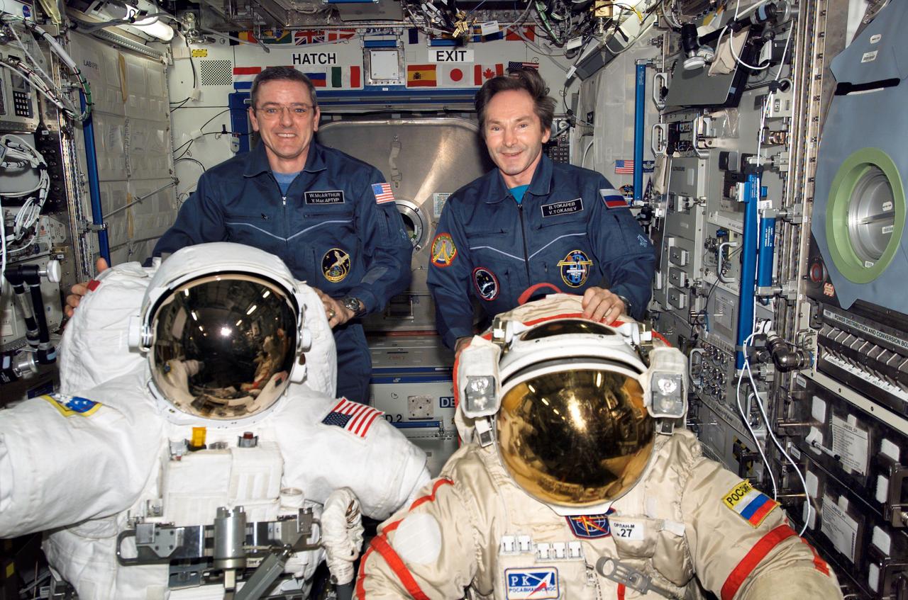 ISS012-E-19194 (5 March 2006) --- Astronaut William S. (Bill) McArthur (left), Expedition 12 commander and NASA space station science officer, and cosmonaut Valery I. Tokarev, flight engineer representing Russia's Federal Space Agency, pose with a U.S. Extravehicular Mobility Unit (EMU) spacesuit (left) and Russian Orlan spacesuit in the Destiny laboratory of the International Space Station.