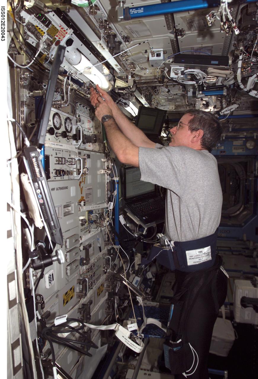 ISS012-E-20043 (9 March 2006) --- Astronaut William S. (Bill) McArthur, Expedition 12 commander and NASA space station science officer, sets up the electromyography (EMG) calibration cord assembly for a data collection session of the Foot/Ground Reaction Forces During Spaceflight (FOOT) experiment in the Destiny laboratory of the International Space Station. McArthur was attired in the specially instrumented Lower Extremity Monitoring Suit (LEMS), cycling tights outfitted with sensors for the experiment.