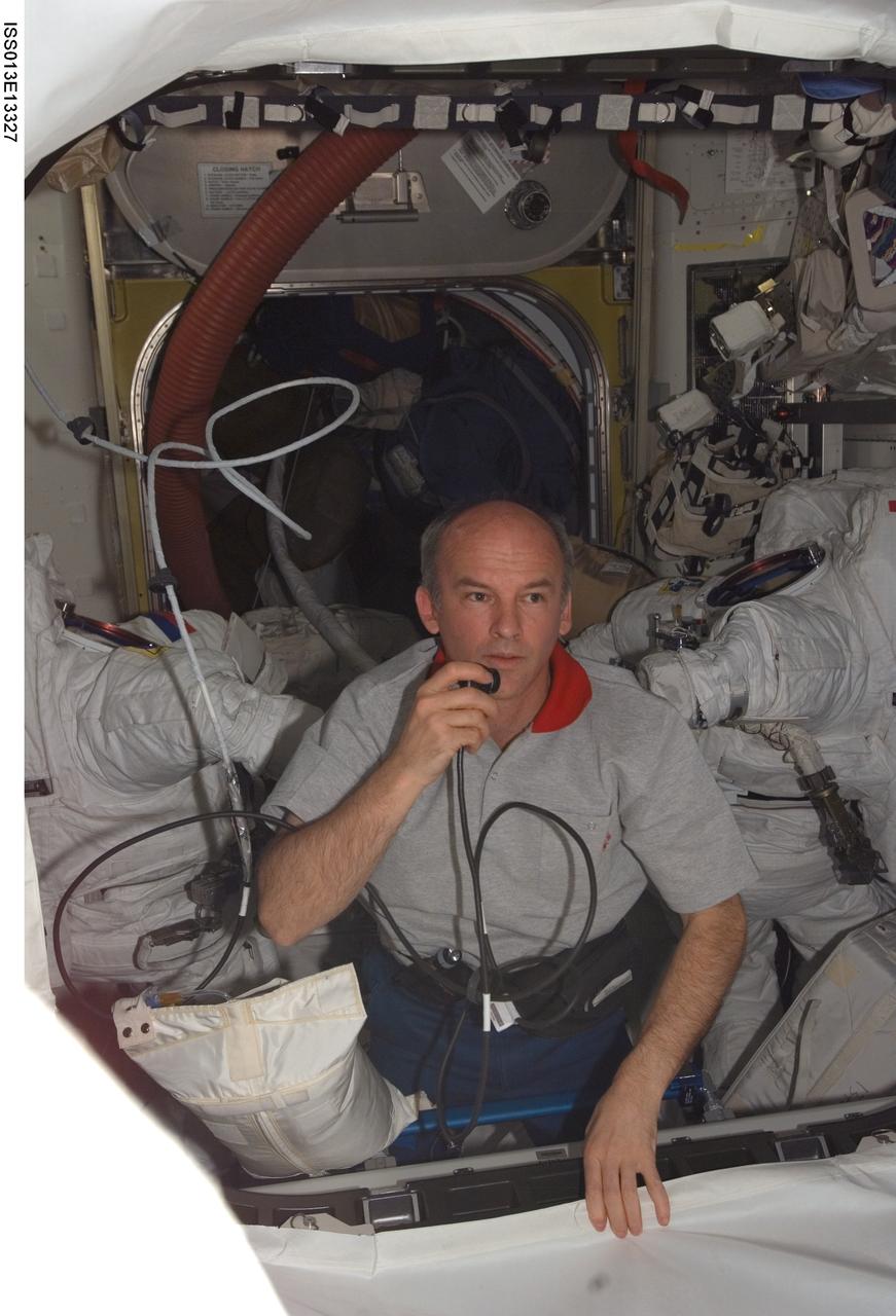 ISS013-E-13327 (1 May 2006) --- Astronaut Jeffrey N. Williams, Expedition 13 NASA space station science officer and flight engineer, uses a communication system in the Quest Airlock of the International Space Station. Two Extravehicular Mobility Unit (EMU) spacesuits are visible in the background.