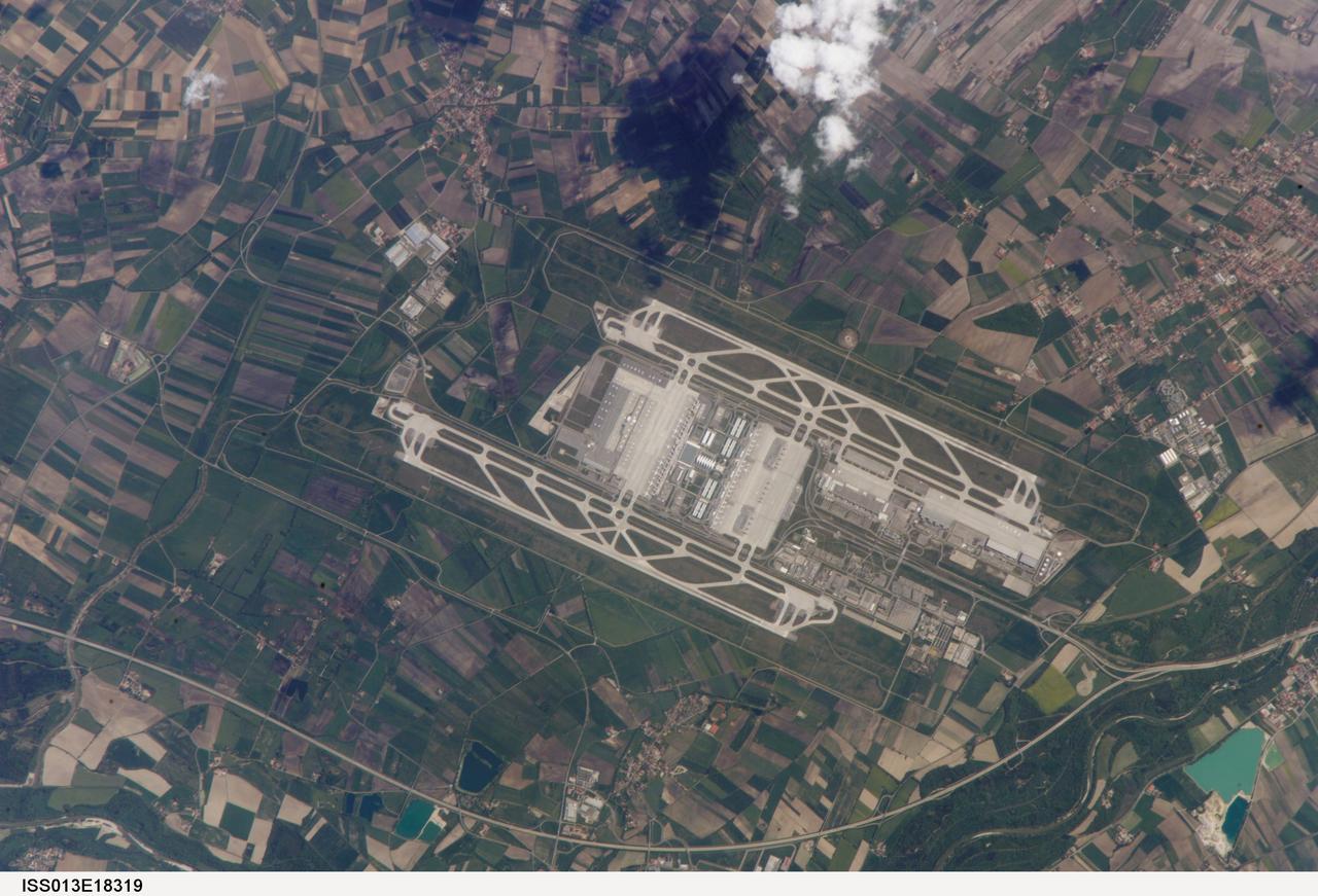 ISS013-E-18319 (12 May 2006) --- Munich International Airport, Germany is featured in this image photographed by an Expedition 13 crewmember on the International Space Station. The Franz Joseph Strauss, or Munich, International Airport served 29 million passengers in 2005, making it the second-busiest airport (behind Frankfurt) in Germany. It is the busiest airport in Germany in terms of domestic passengers, serving over 9 million travelers during 2005. The airport serves the Bayern (Bavaria) region of southeastern Germany, and is a hub for the Lufthansa airline. Like other large international airports around the world, the facility occupies portions of multiple municipalities: Freising, Oberding, Hallbergmoos, and Marzling. The village of Franzheim was demolished, and its 500 residents relocated, during the airport construction. The airport is located 31 kilometers to the northeast of Munich; rather than being an extension of the metropolis, it is surrounded by agricultural fields and small towns. Expansion of the airport occurred in 2003 with the additional of Terminal 2, designed specifically to accommodate the needs of Lufthansa and its partner airlines. This view taken is sufficiently detailed to distinguish individual airplanes on the terminal apron as well as the dark gray-blue rooftop of Terminal 2. The white concrete airport runways are 4 kilometers in length. Surrounding agricultural fields in active use are a variety of shades of green, while the exposed soil of fallow fields are brown to tan.