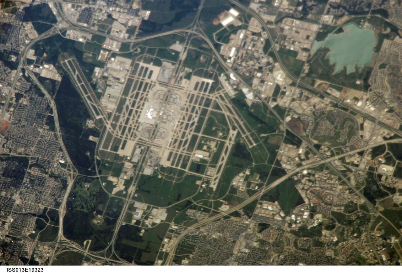ISS013-E-19323 (13 May 2006) --- The largest airport in Texas, Dallas-Fort Worth (DFW) International Airport, is featured in this image photographed by an Expedition 13 crewmember on the International Space Station. DFW is also the fourth largest in the world, and occupies more surface area than the entire island of Manhattan in New York. The airport is officially owned by the cities of Dallas and Fort Worth, but is sited within the city limits of four neighboring cities (Coppell, Euless, Grapevine, and Irving). This oblique image captures the entire airport and portions of the surrounding Dallas-Forth Worth metropolitan area. The white rooftops of the new - completed in 2005 - International Terminal D are also distinct from less reflective rooftops of the older terminals. A sense of the size of the airport is provided by the approximately 2,800 meters long northwest-southeast oriented runway to the west of Terminal D. The oblique viewing angle also accentuates light reflection off of North Lake (image upper right), giving the water surface a grey-green cast.